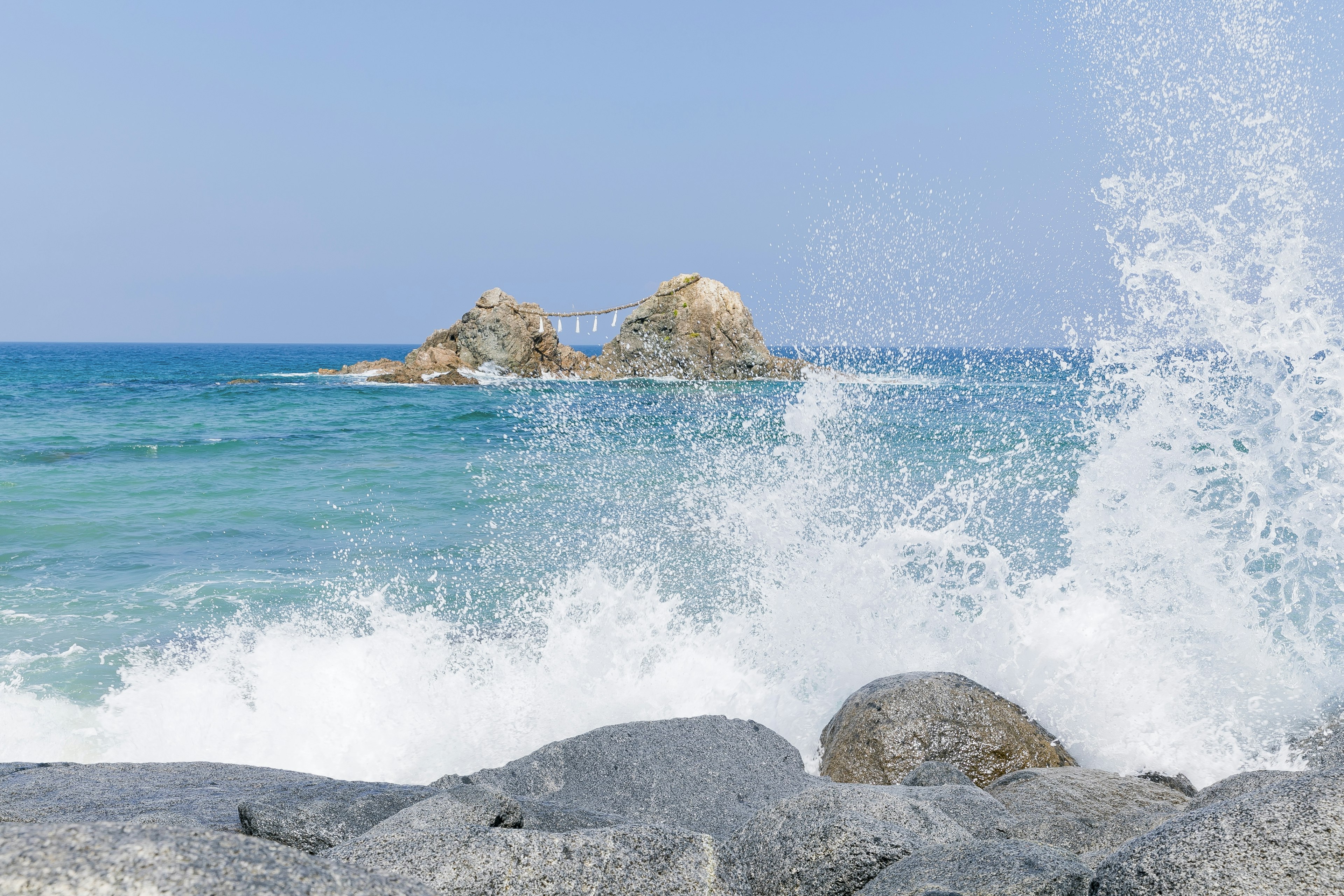 Waves crashing against rocks with a distant island in a blue sea