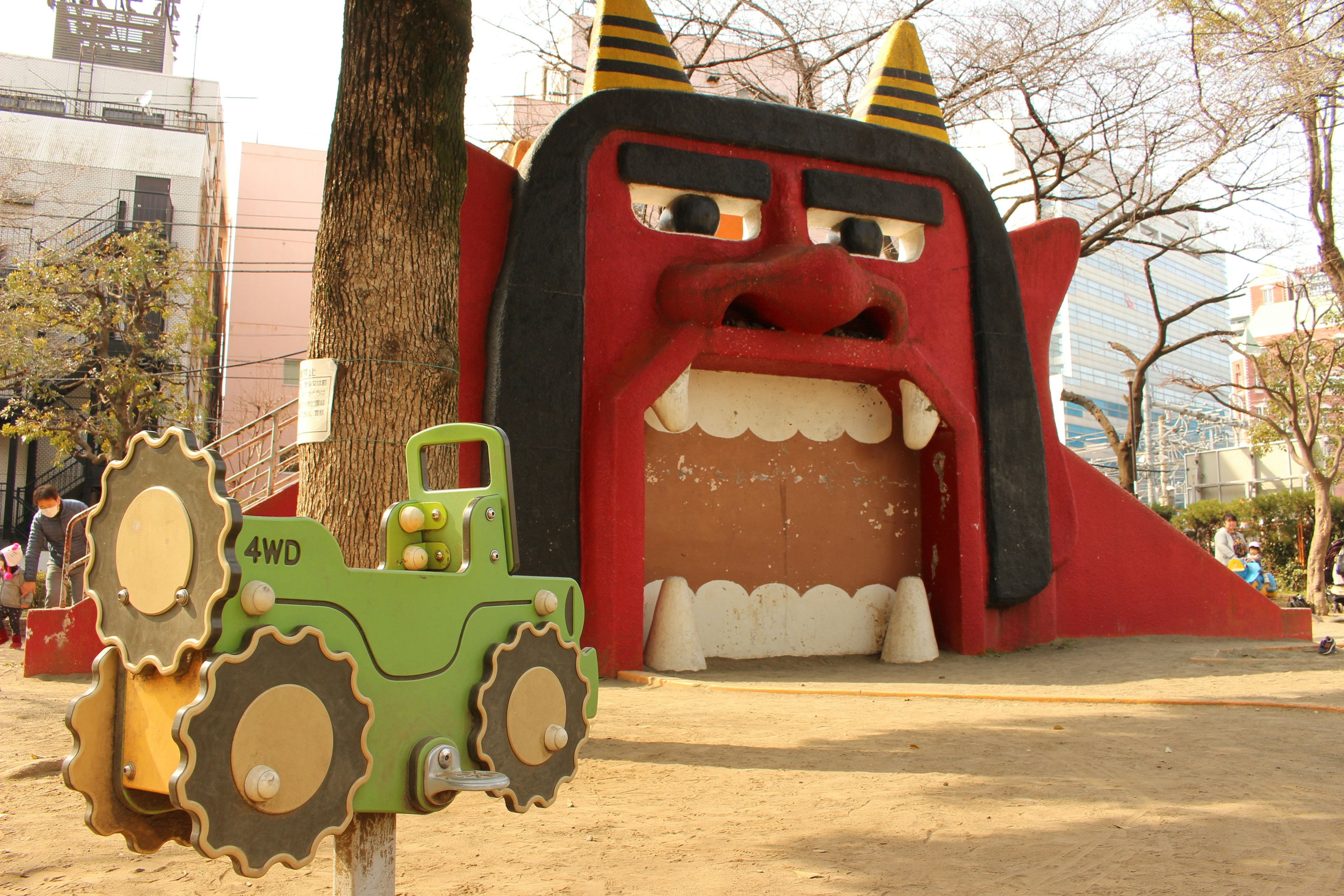 Parque infantil con un gran rostro de demonio rojo y un tractor de juguete verde