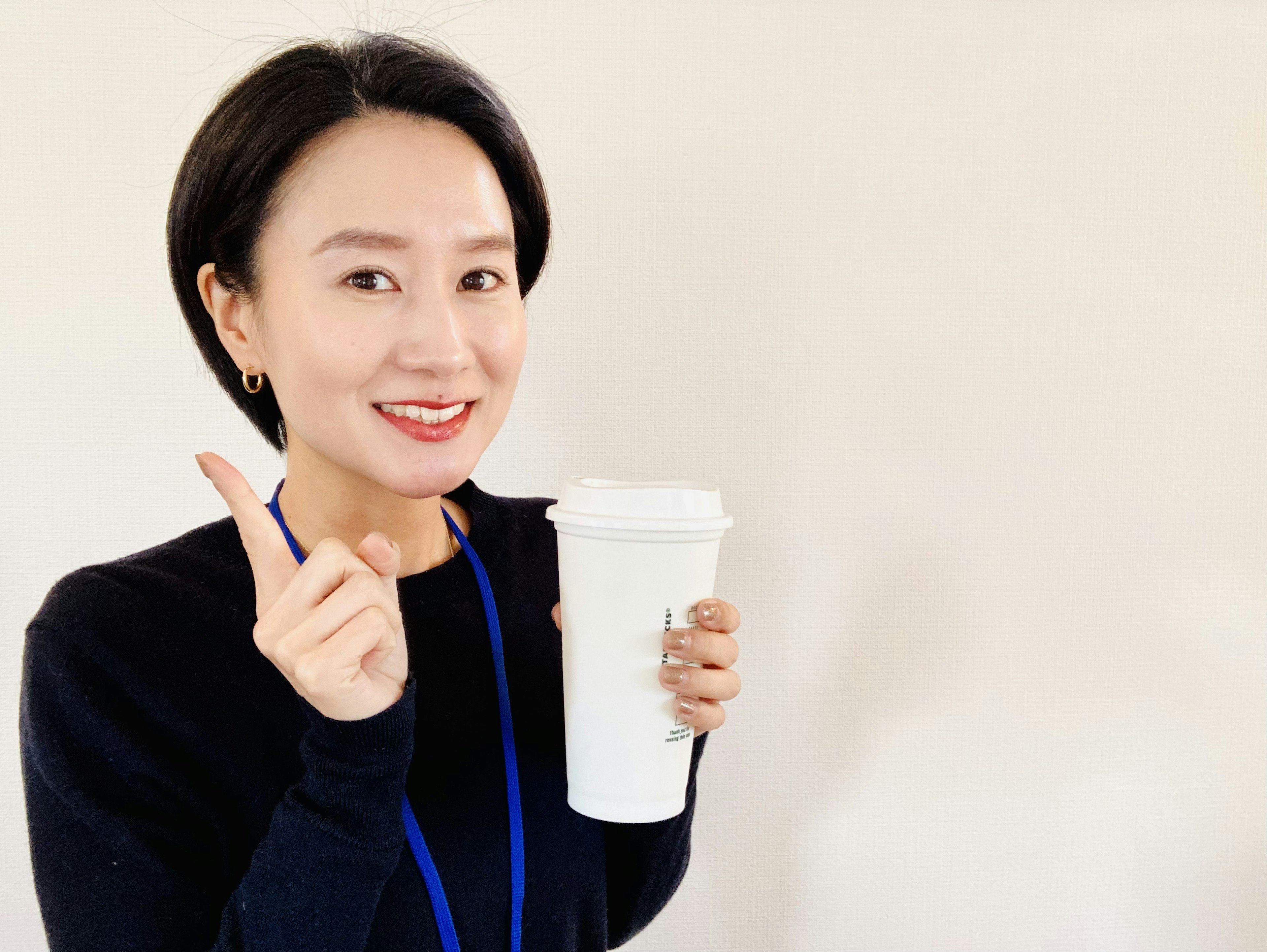 Femme souriante tenant une tasse blanche et pointant avec son doigt