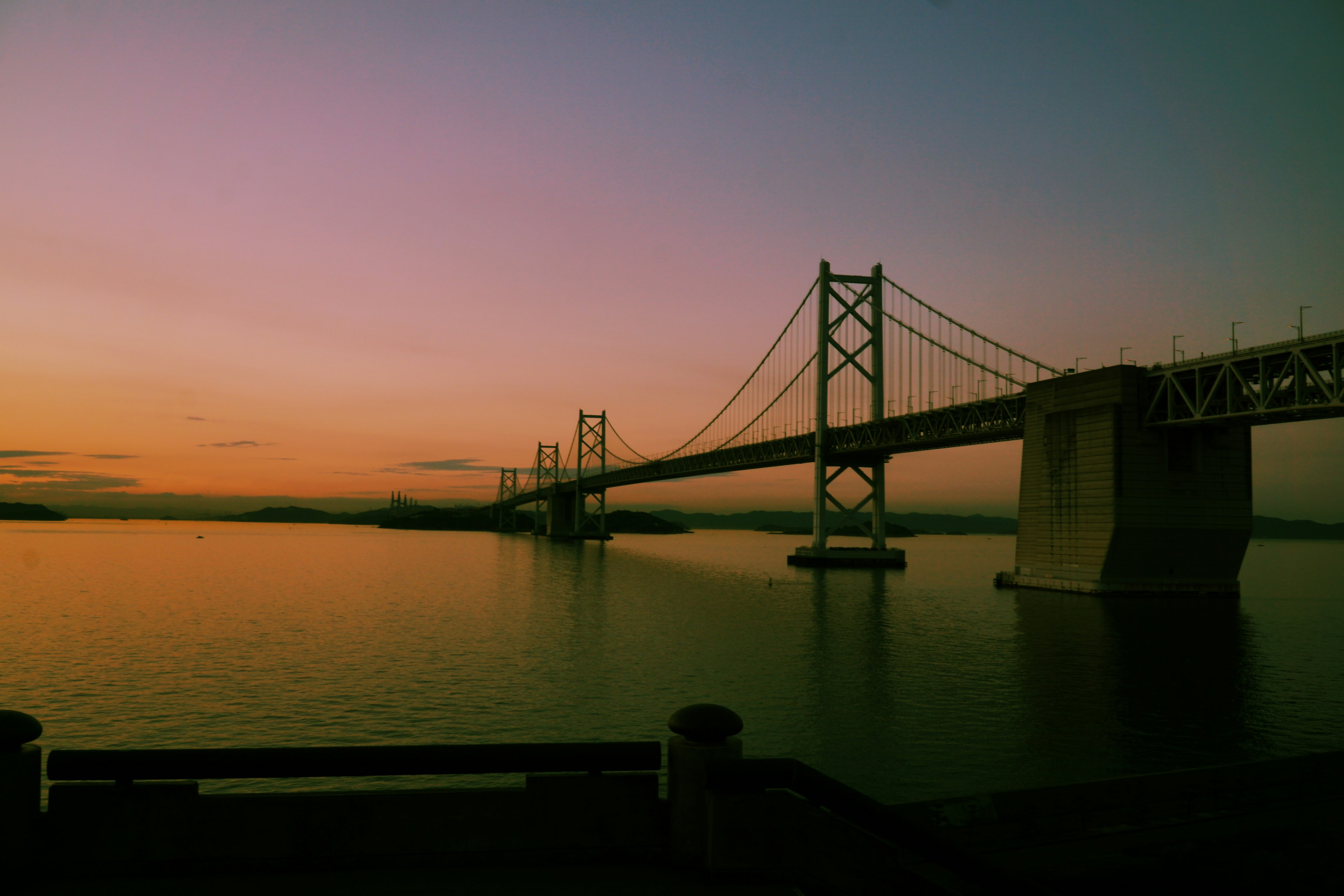 Bridge spanning a calm river at sunset with colorful sky