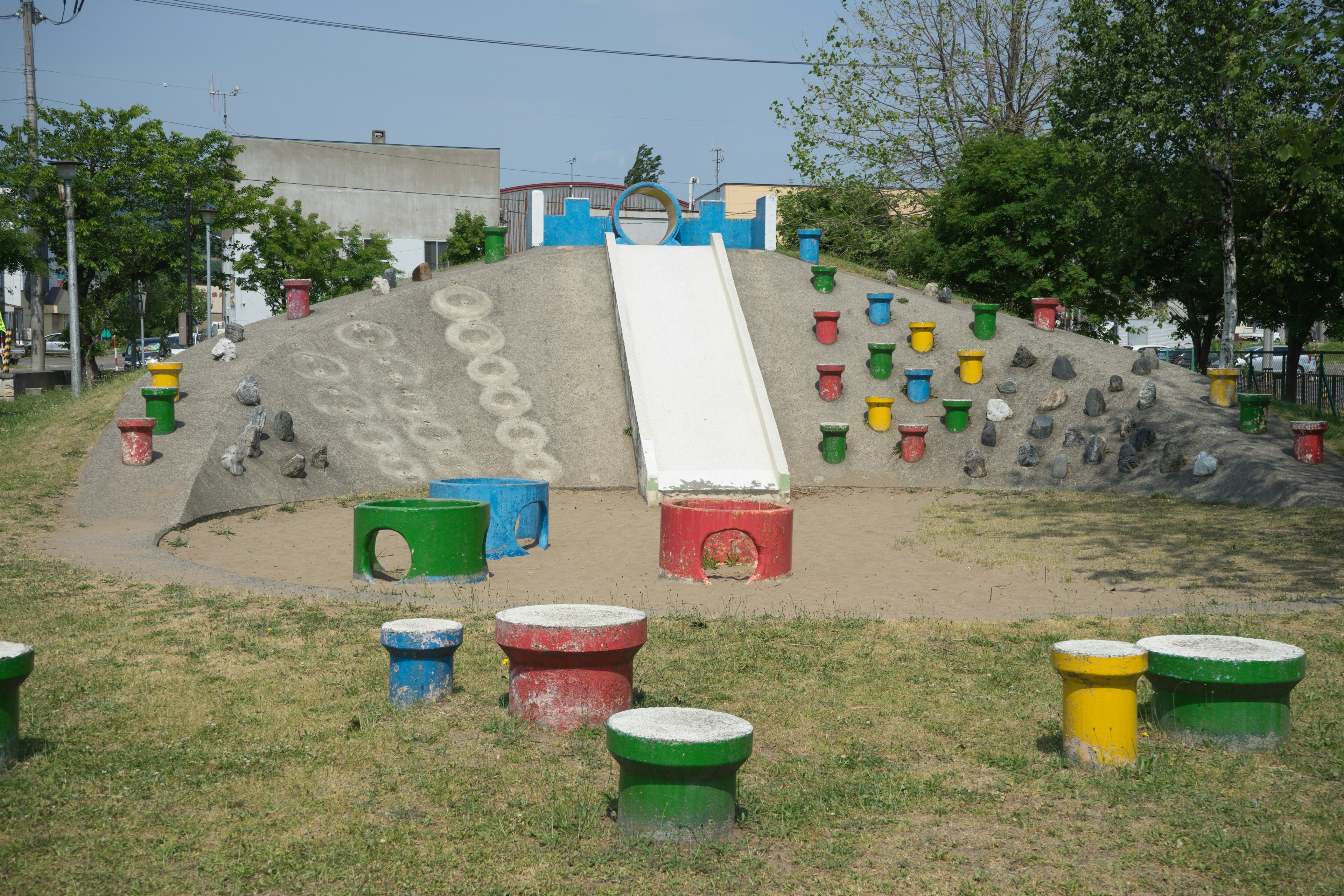 Escena de parque infantil con un tobogán colorido en una colina de arena rodeada de hierba verde