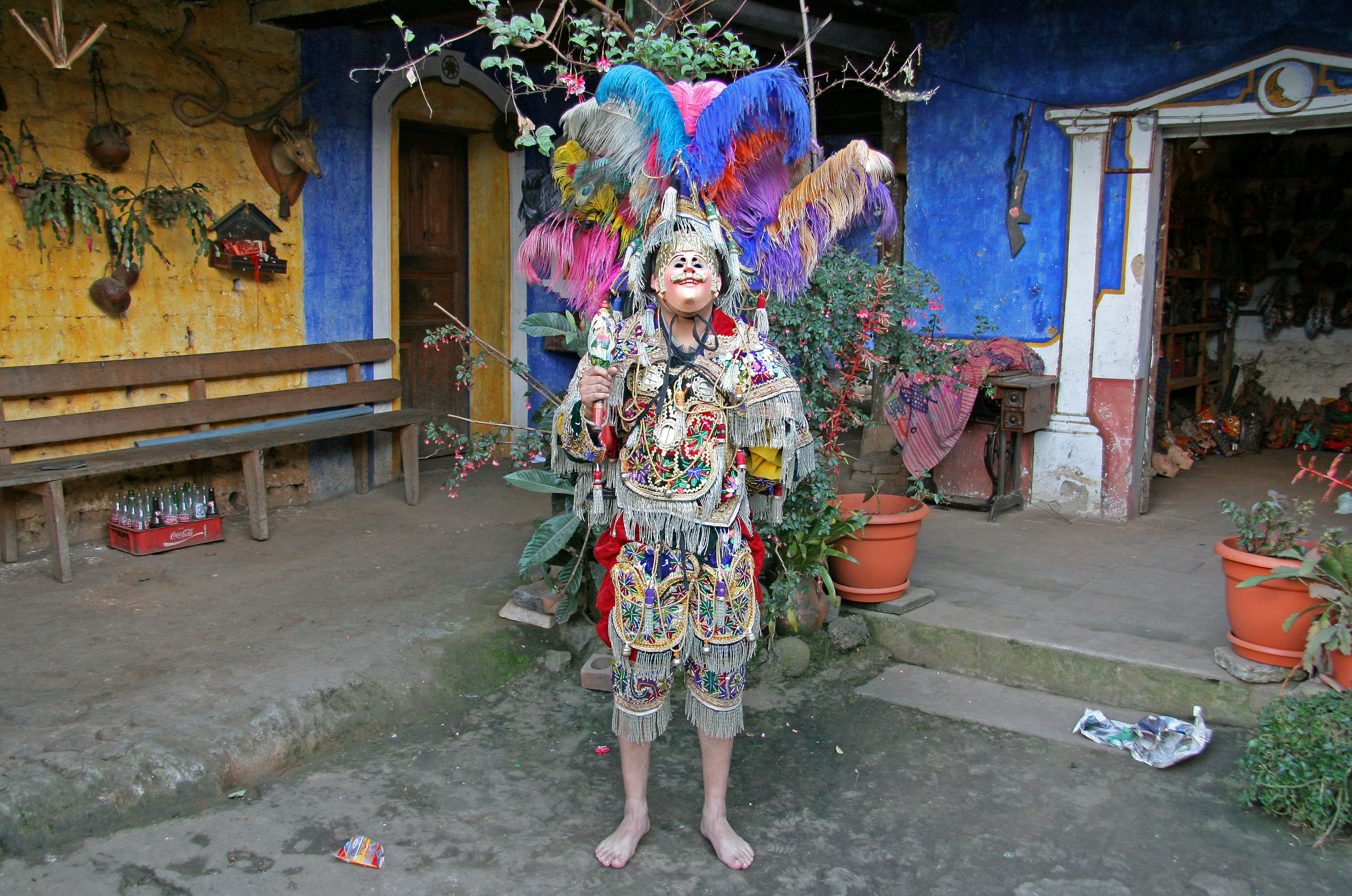 A child dressed in colorful attire stands in a garden with vibrant walls and plants in the background