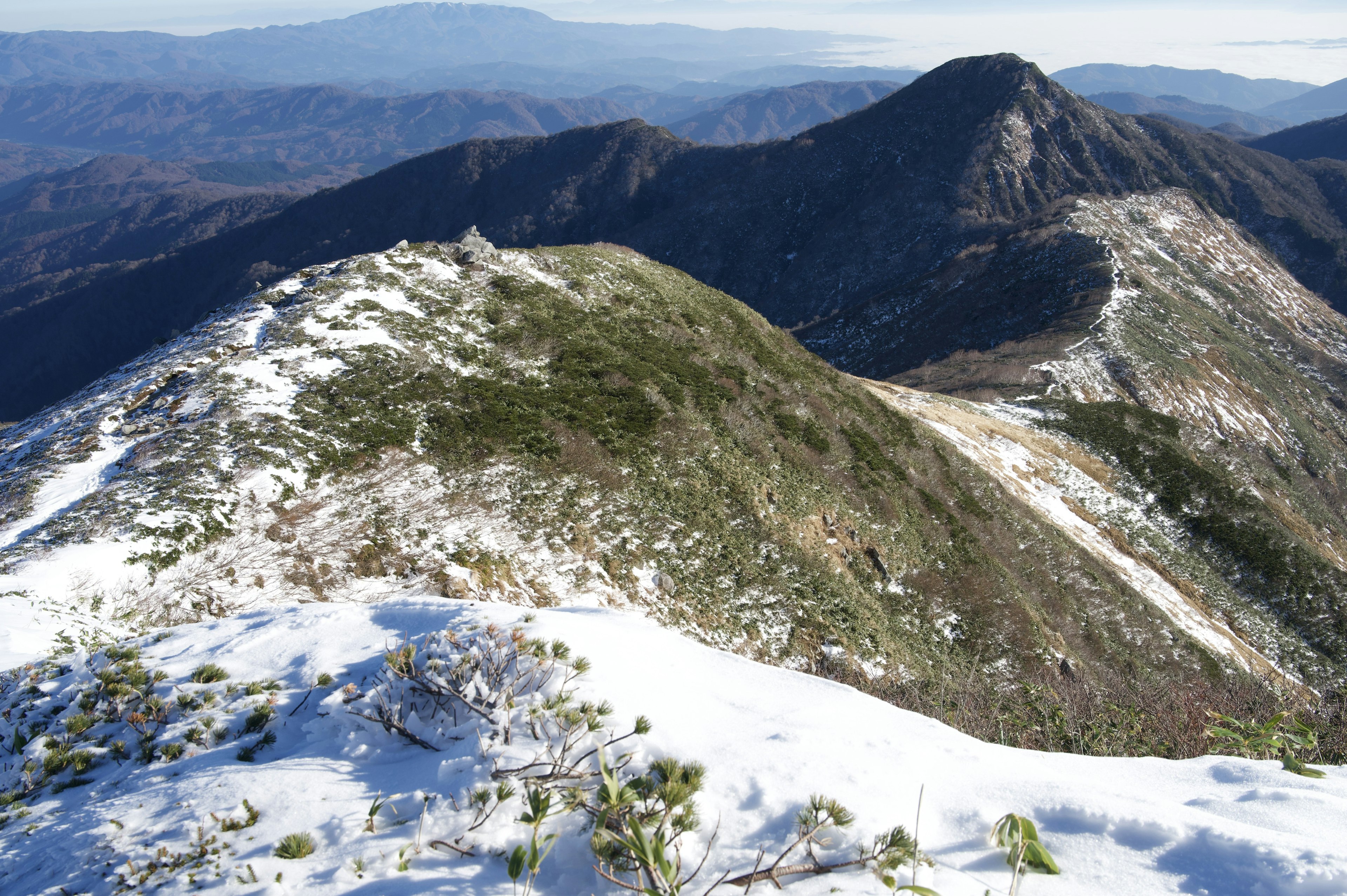 Schneebedeckte Berglandschaft mit üppigen grünen Hängen und fernen Gipfeln