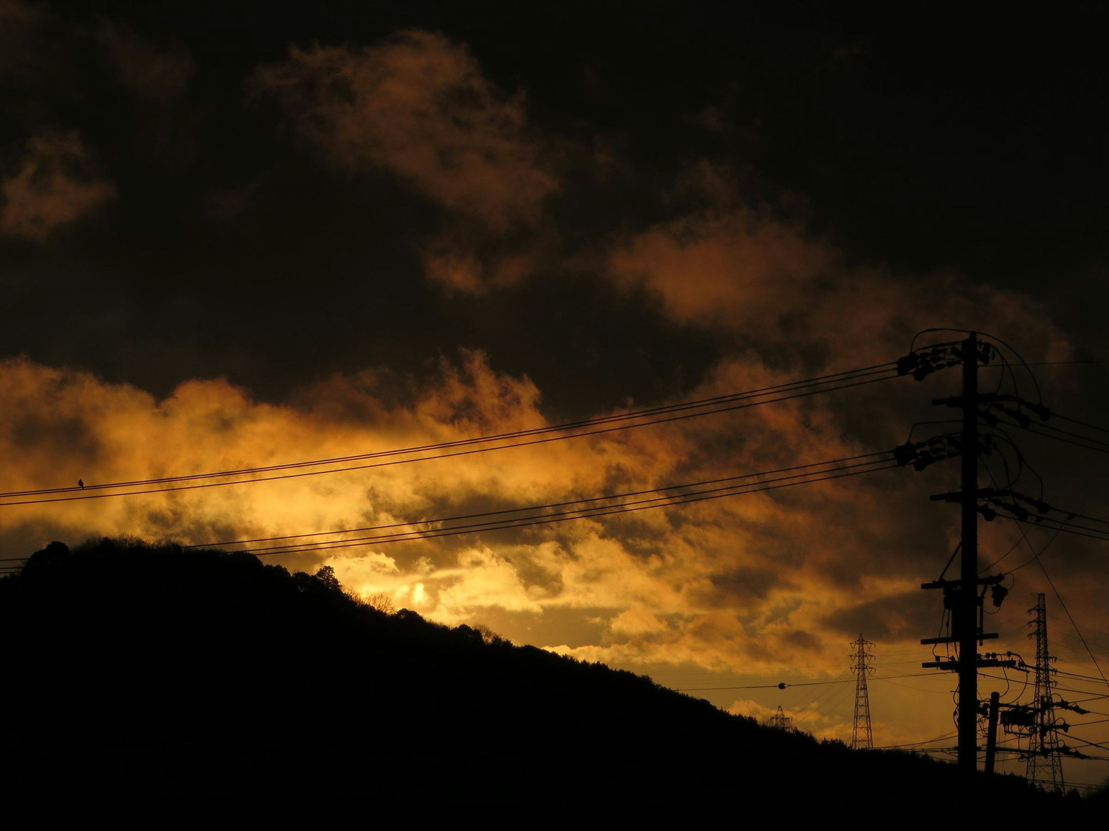 Silhouette of a mountain against a dark sky with clouds and sunset glow