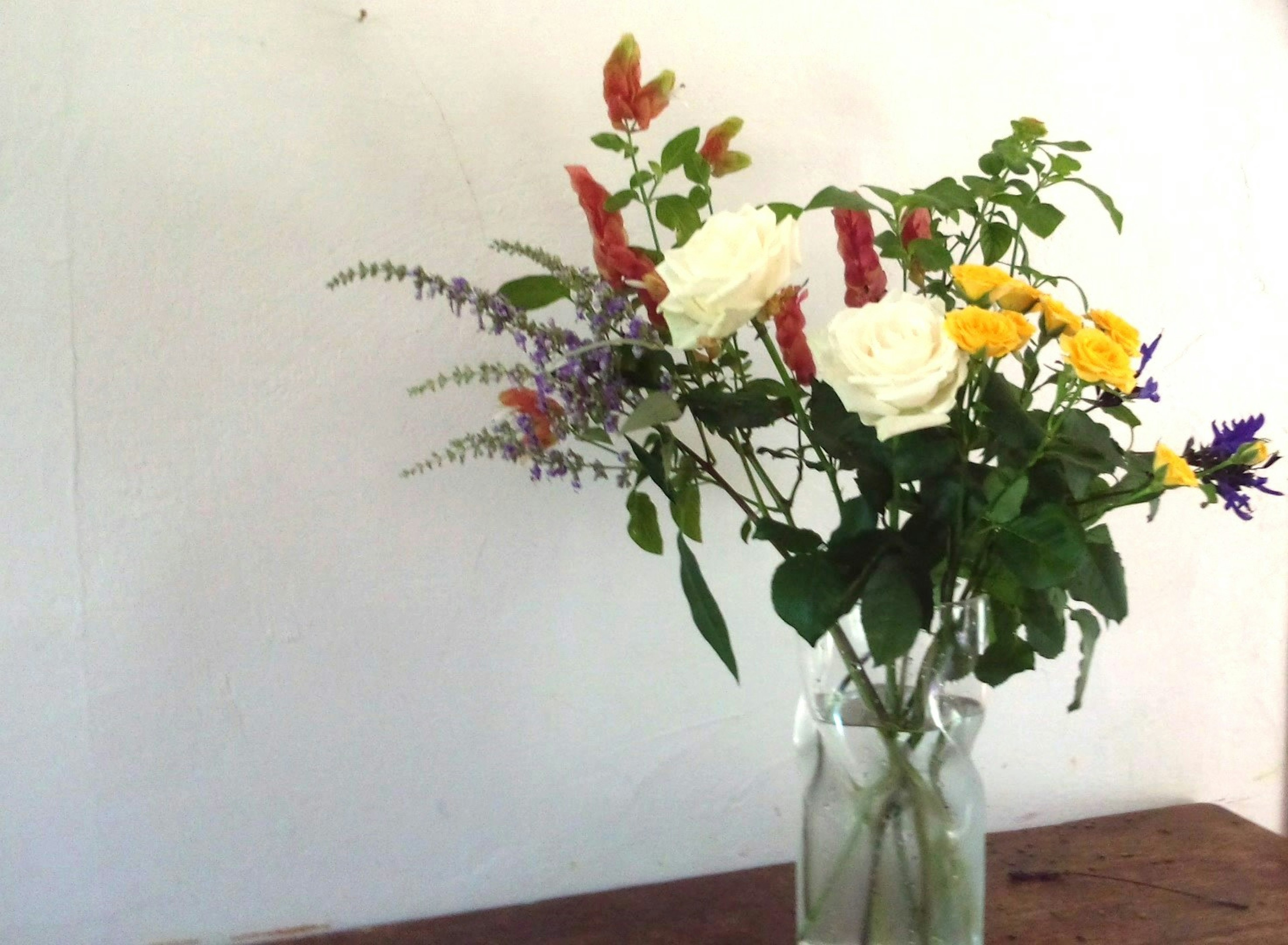 Un vaso trasparente pieno di rose bianche e fiori colorati