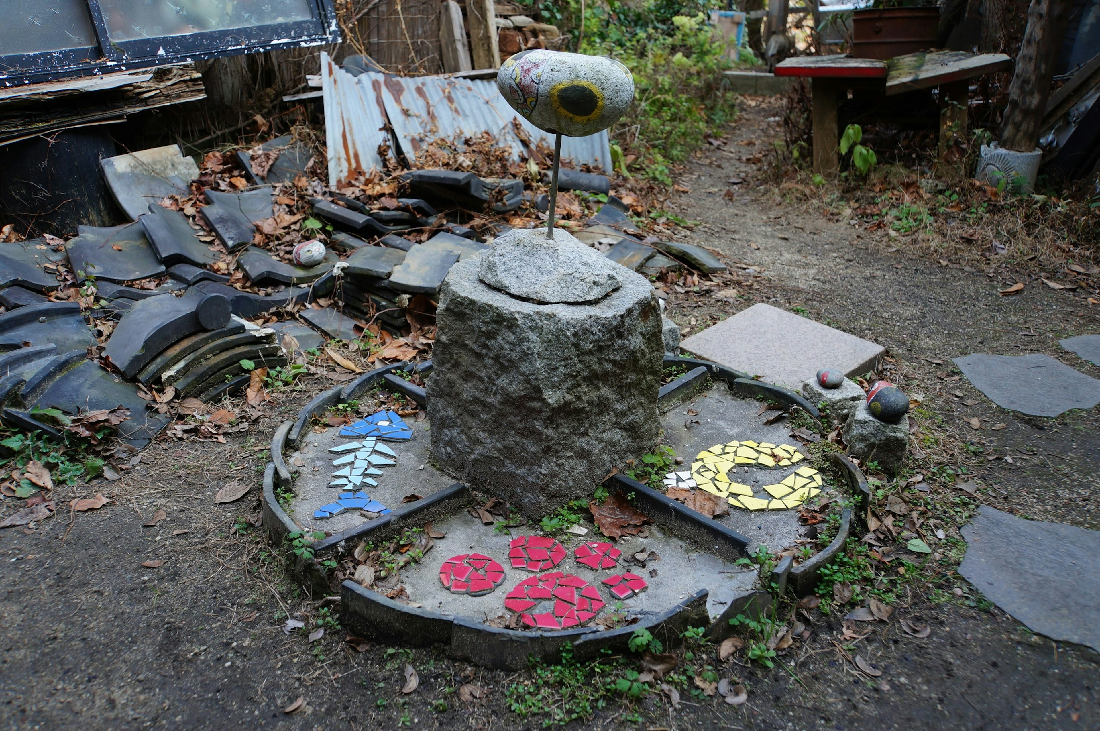 Scultura in pietra con motivi colorati in un giardino circondato da foglie e detriti