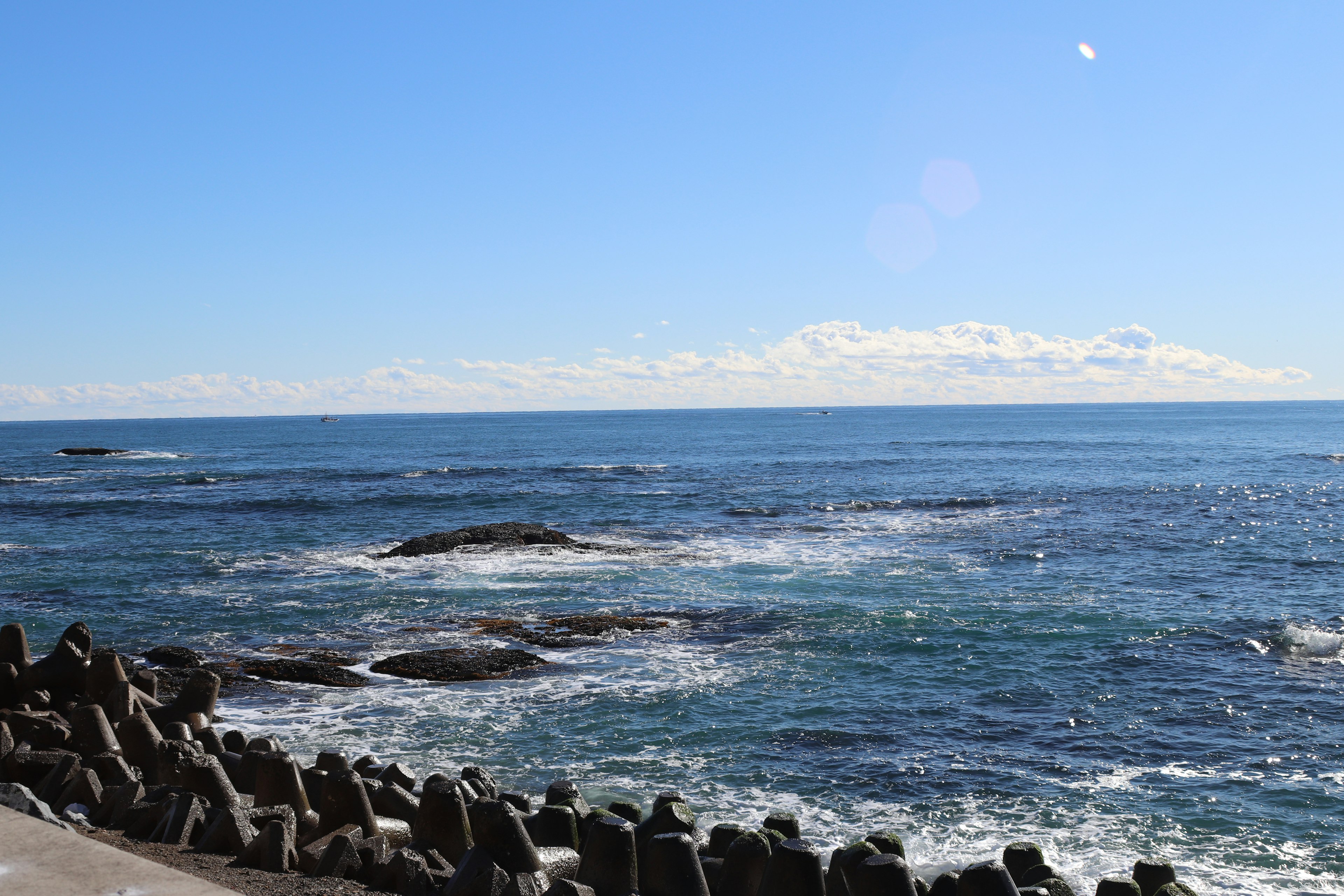 Paesaggio di mare blu e cielo sereno con frangiflutti in pietra visibili