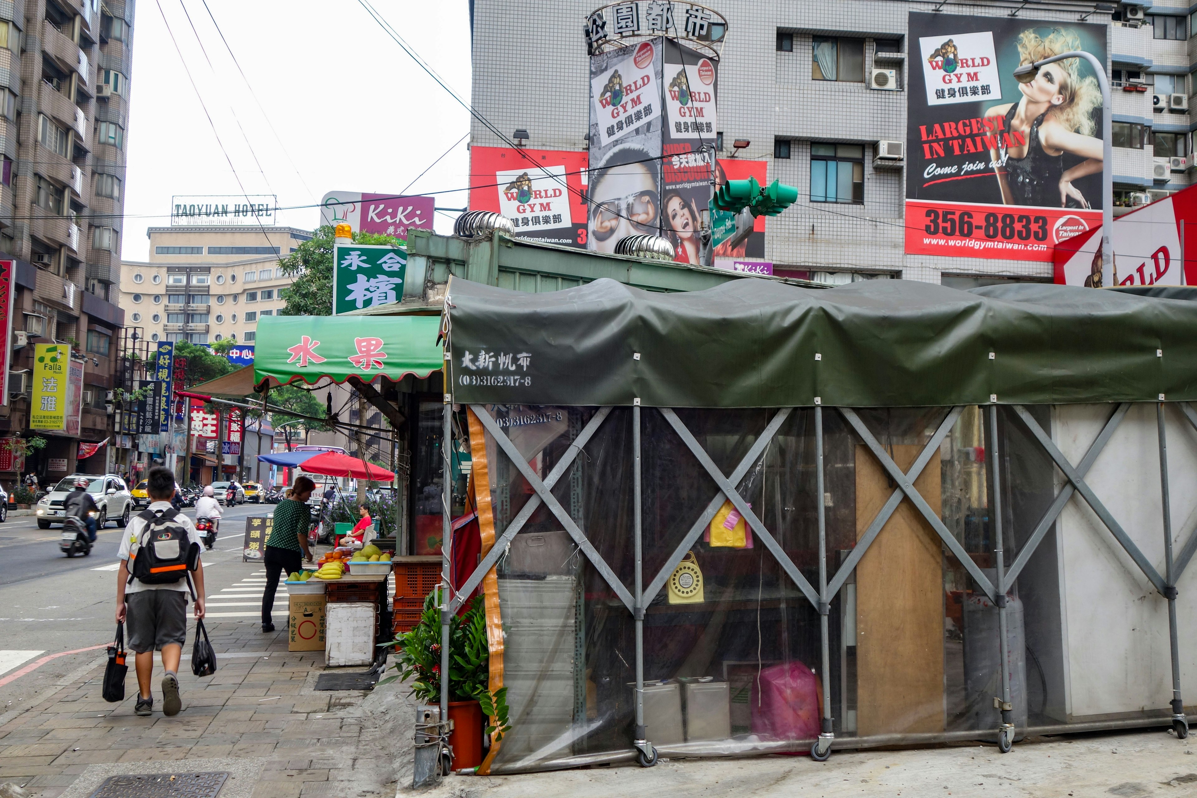 賑やかな街角の風景で、看板や店舗が並ぶ通りに面した緑色のテントが特徴的