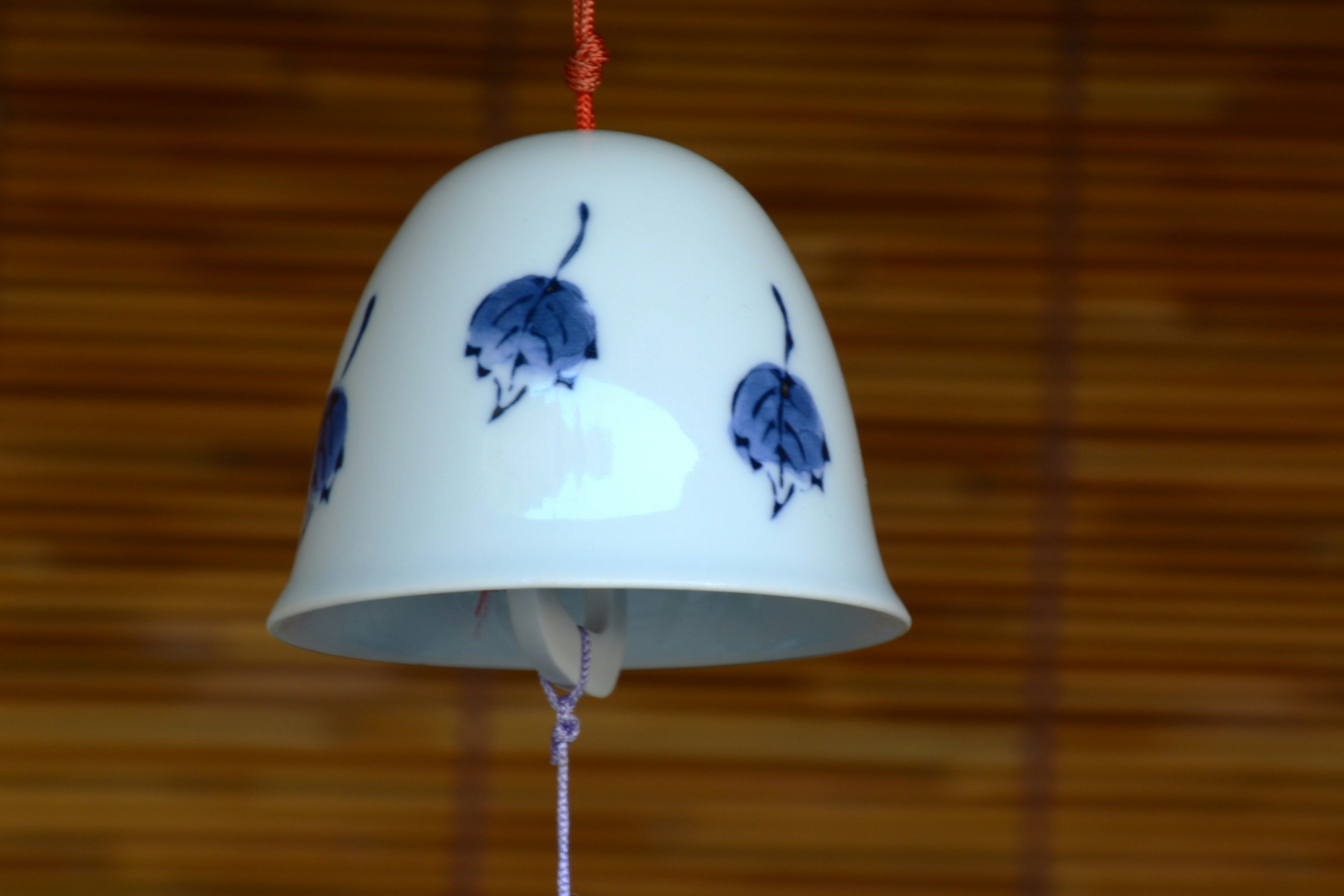 Cloche en céramique blanche avec des motifs floraux bleus suspendue sur un fond en bois