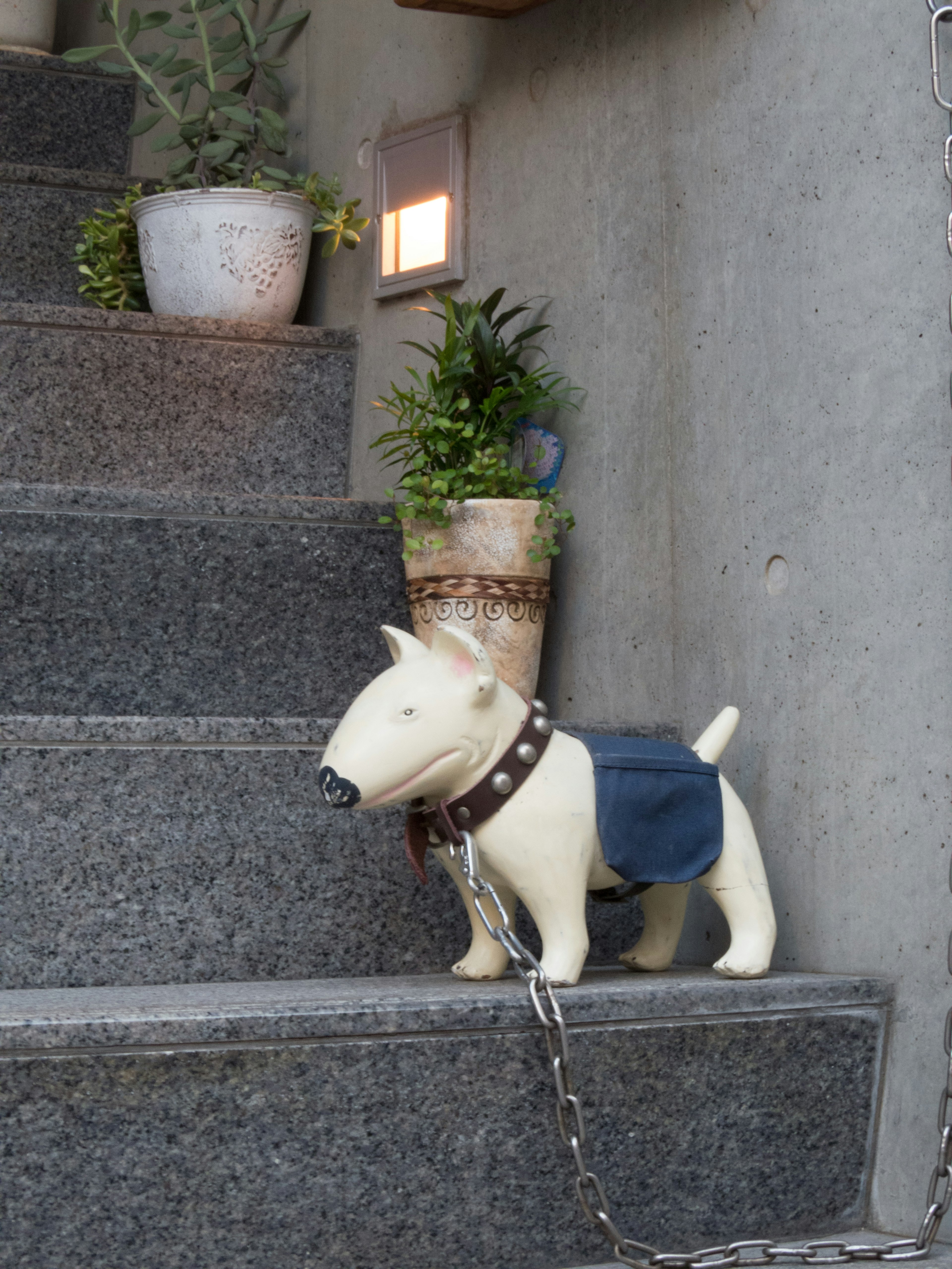 A dog statue standing on stairs with potted plants nearby