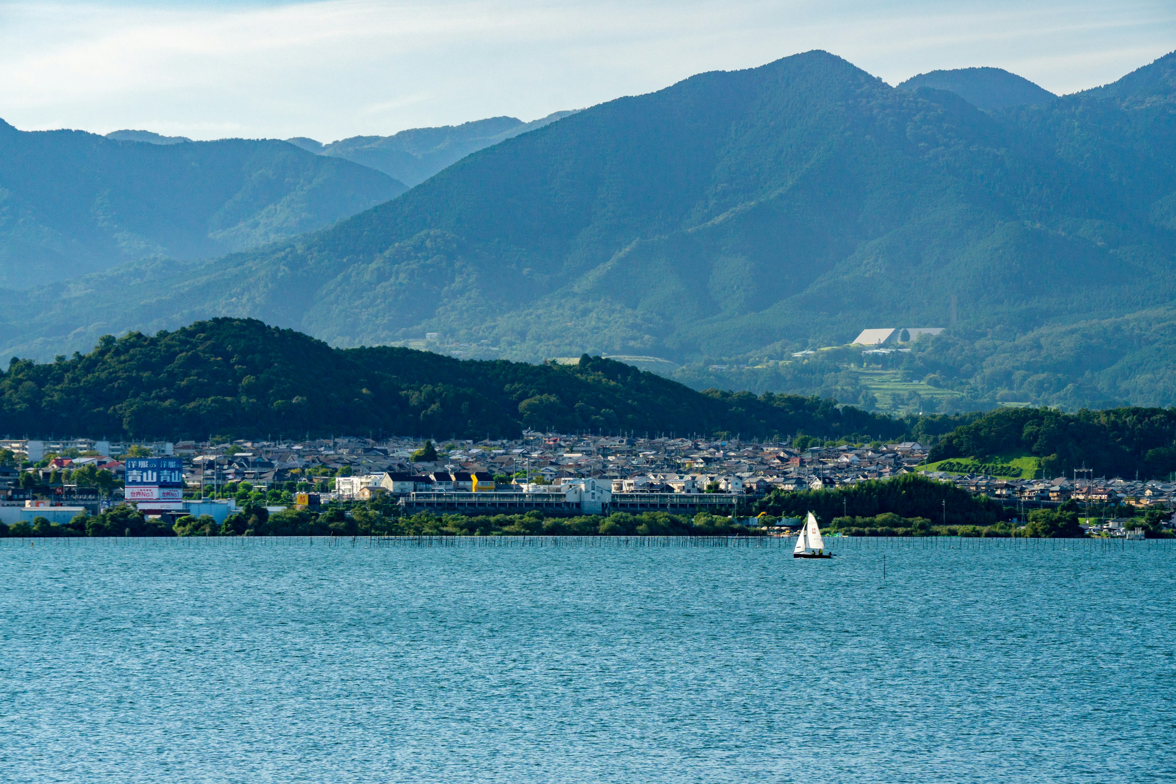 Vista panoramica di un lago blu con montagne sullo sfondo e una piccola barca a vela