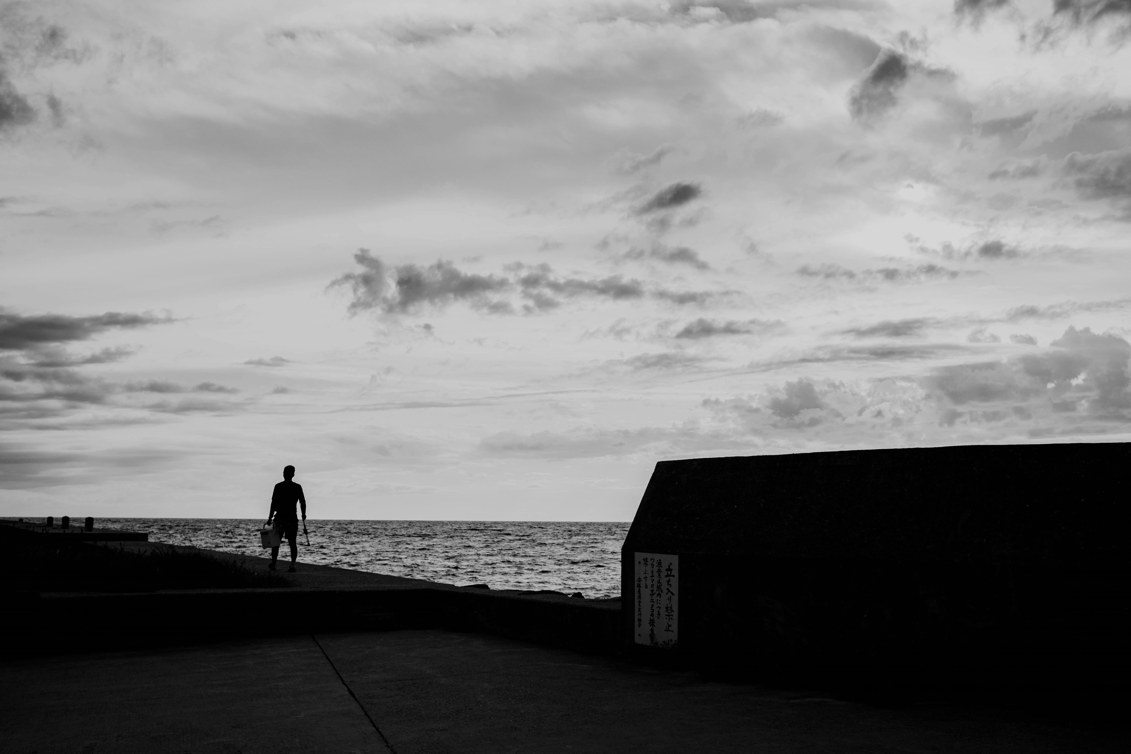 Silhouette einer Person, die am Meer steht, mit dunklen Wolken in einer Schwarz-Weiß-Landschaft