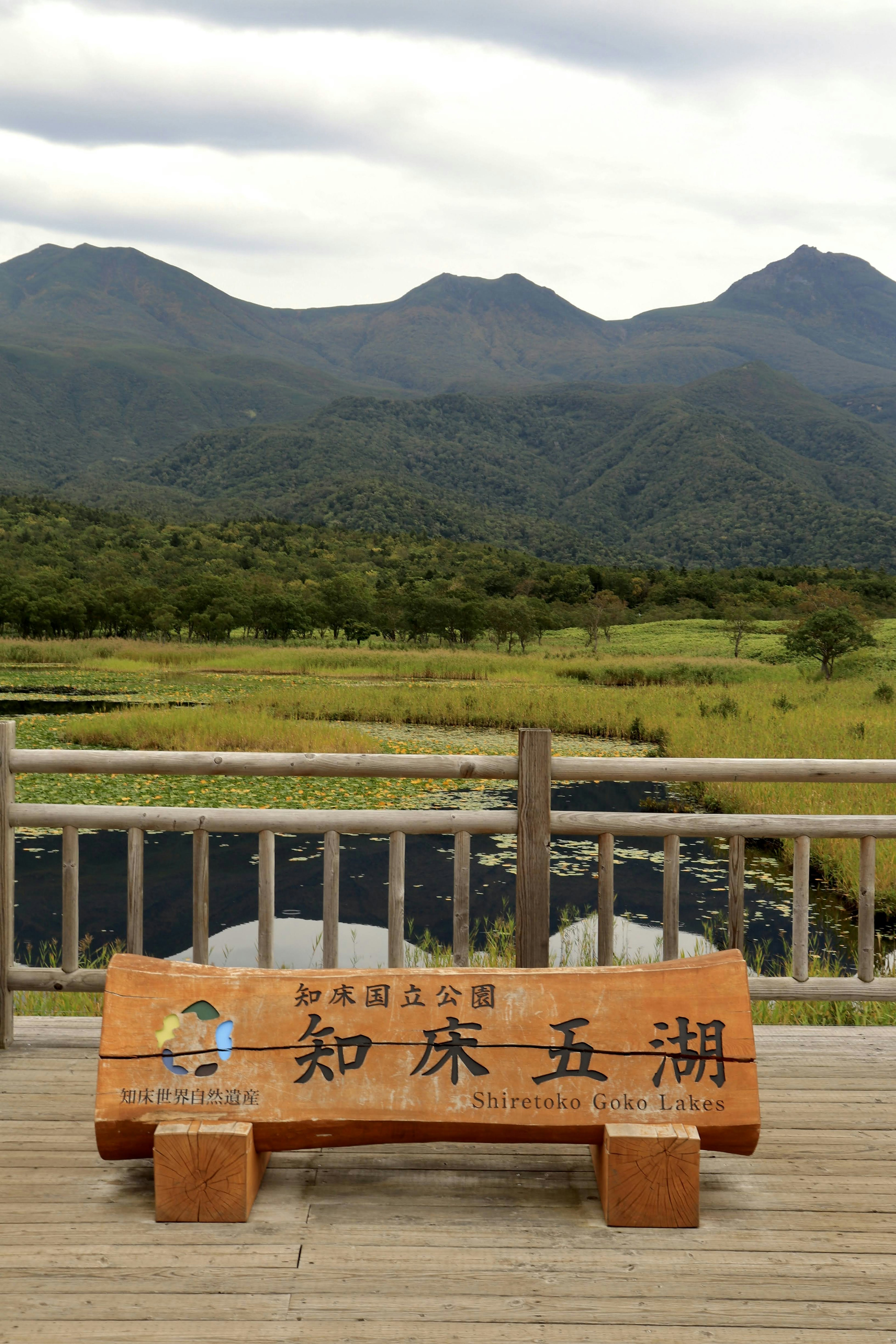 木制标牌上有日文字符，背景为山脉和绿色植被