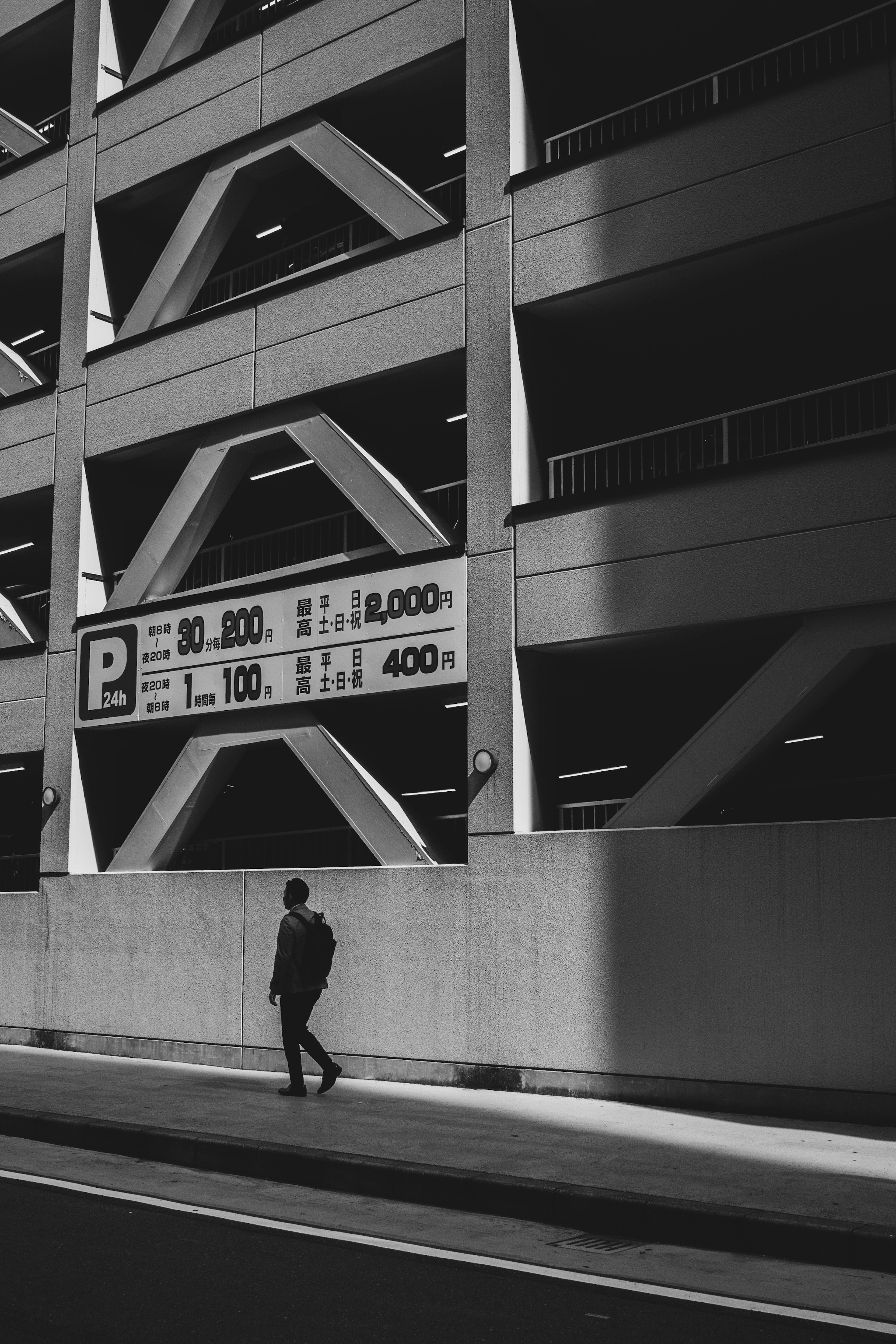 Escena en blanco y negro de una persona caminando junto a un letrero de estacionamiento