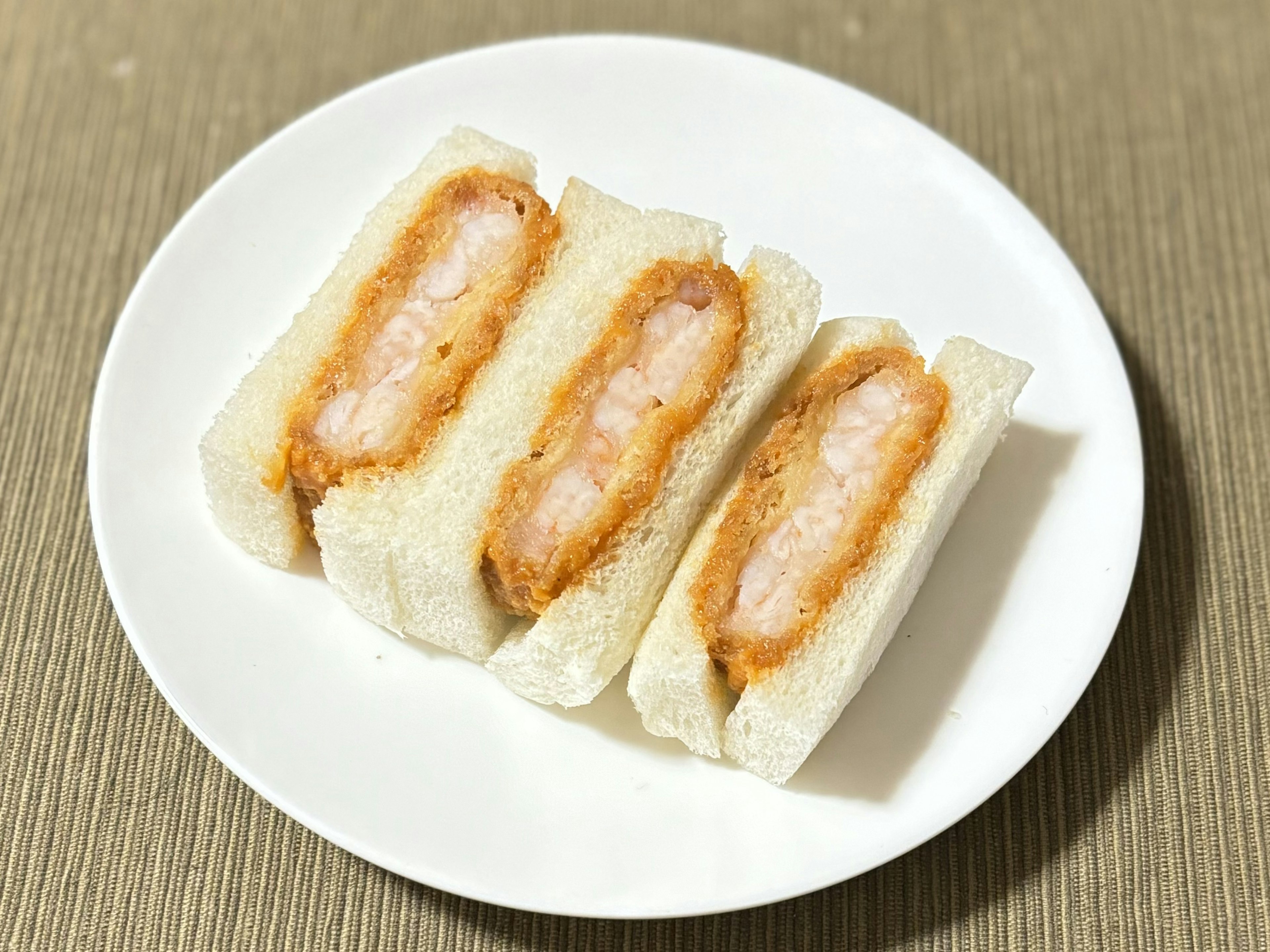 Trois sandwichs aux crevettes sur une assiette blanche avec du pain moelleux