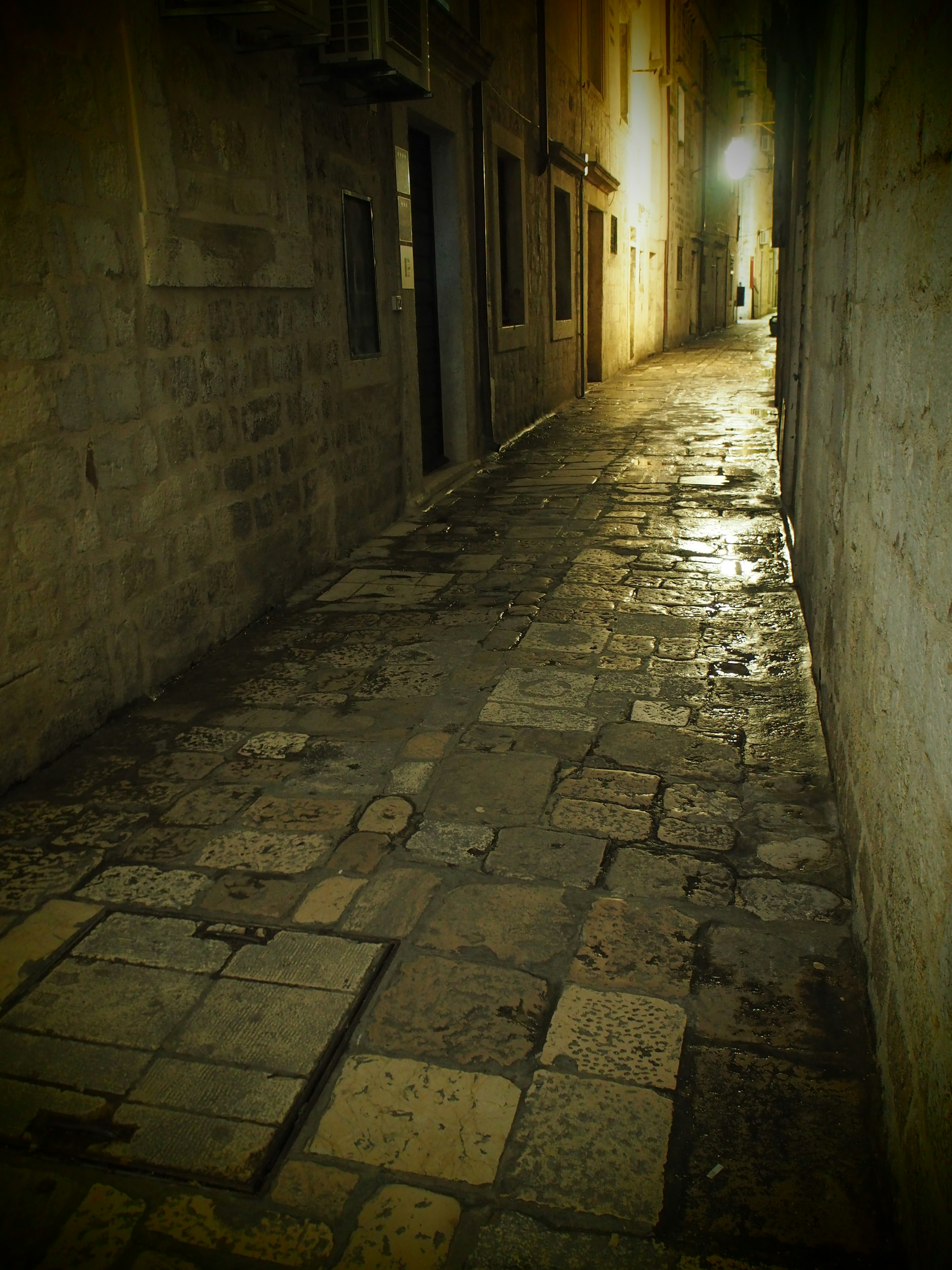 Callejón estrecho de adoquines con paredes desgastadas y luz al final