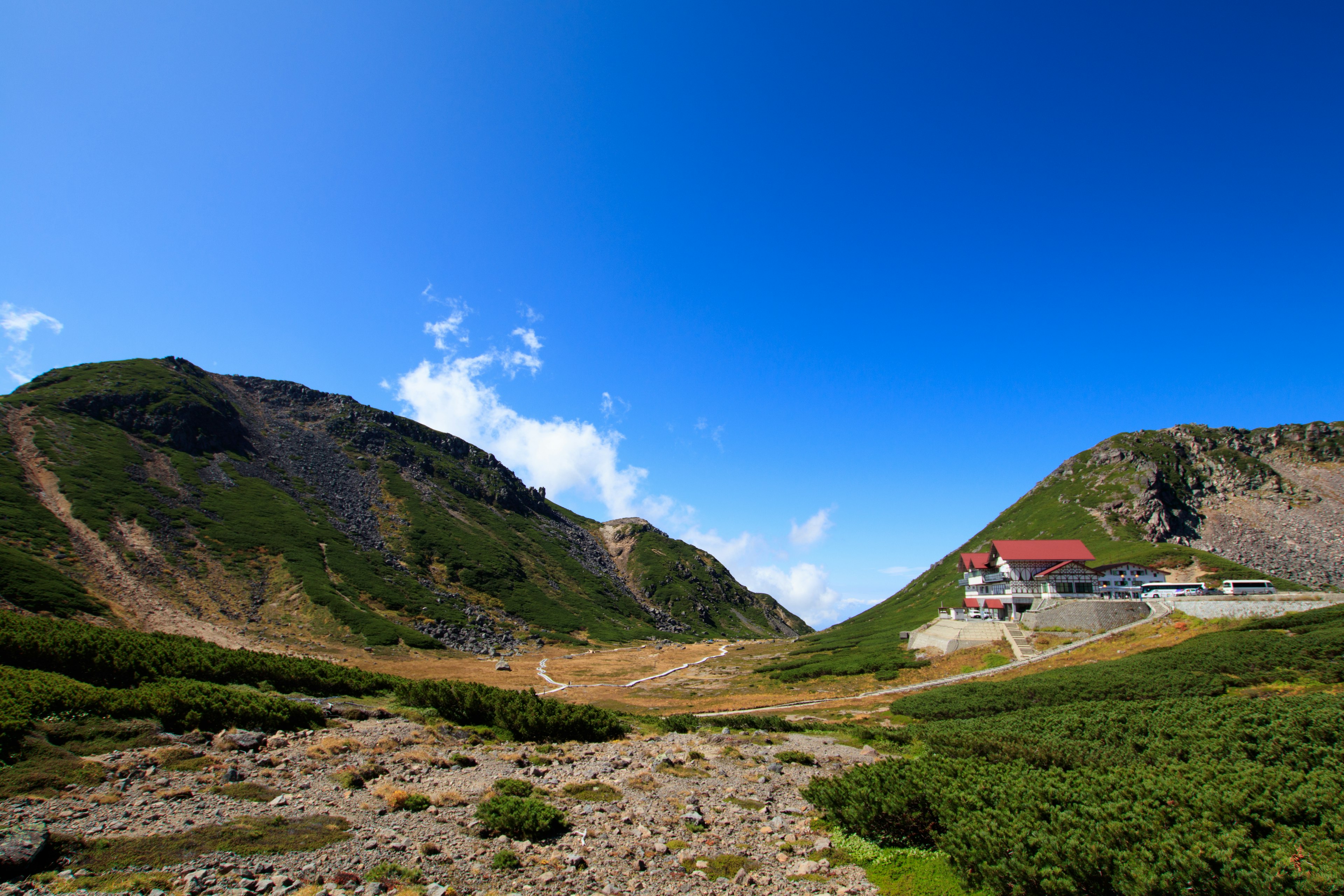 A building nestled in a valley surrounded by green hills and a clear blue sky