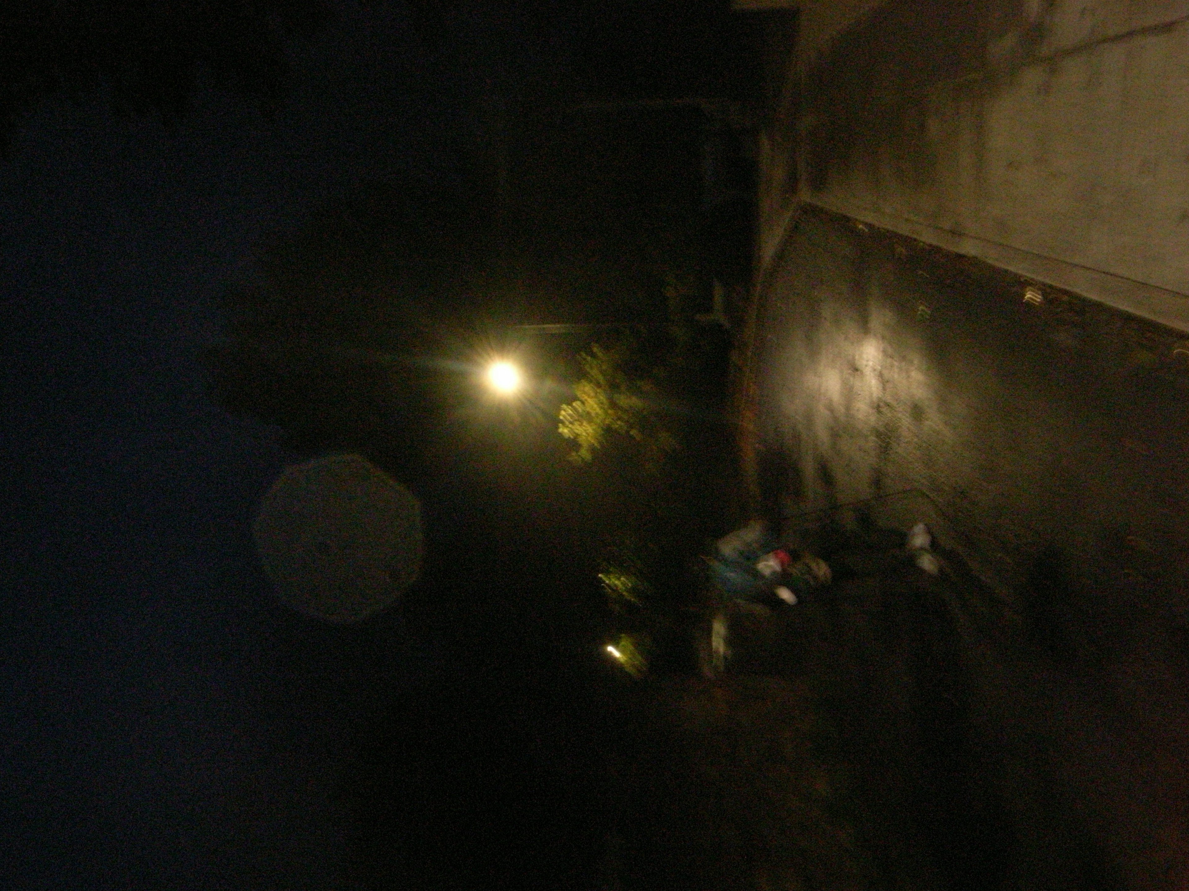 A dark night street illuminated by a streetlight with wet pavement