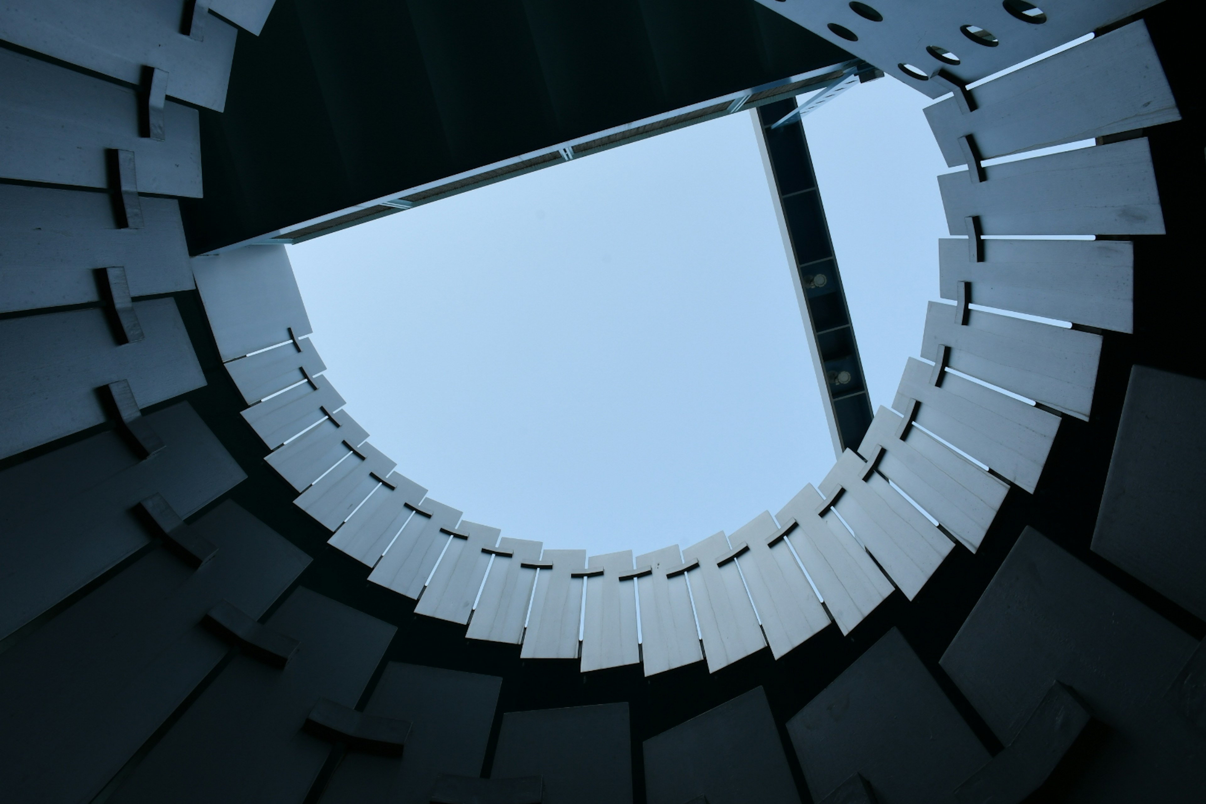 View looking up through a circular structure with white panels framing the sky