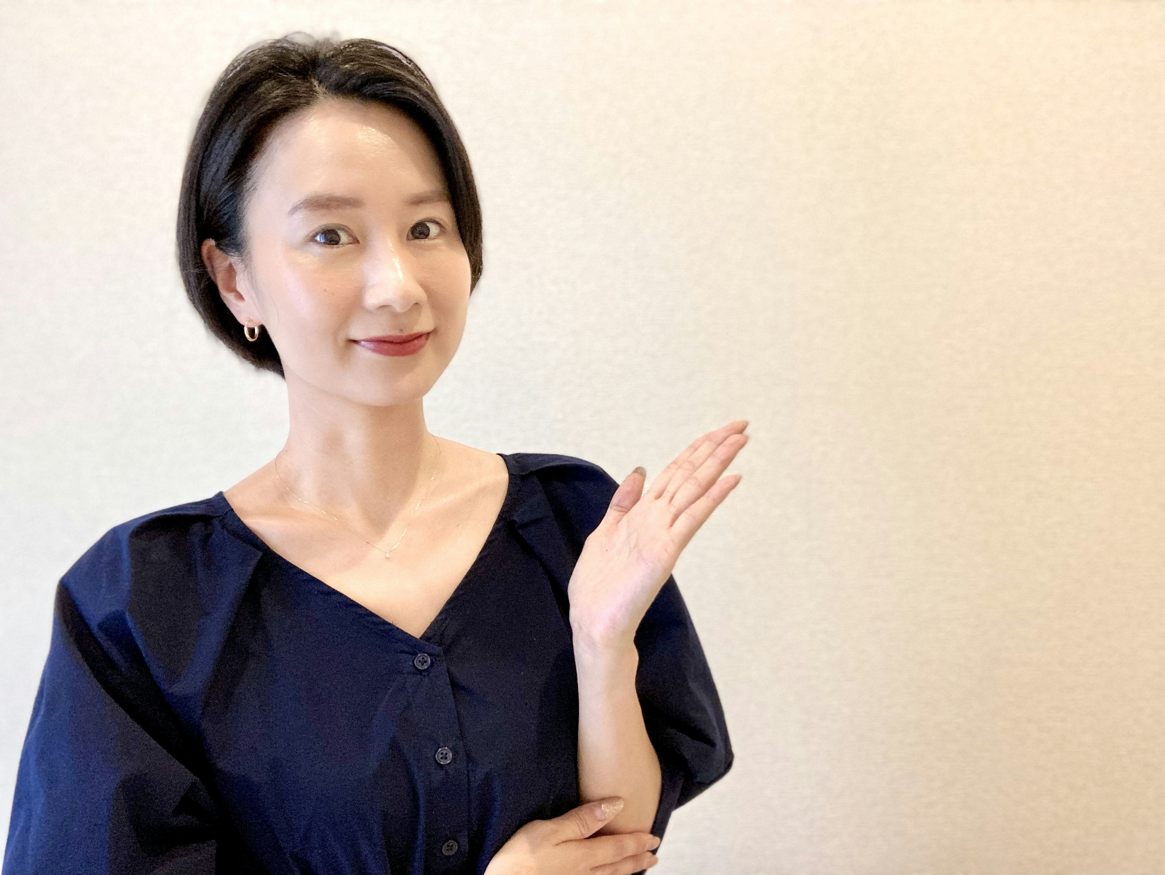 A woman wearing a blue outfit smiling and gesturing with her hand against a simple background