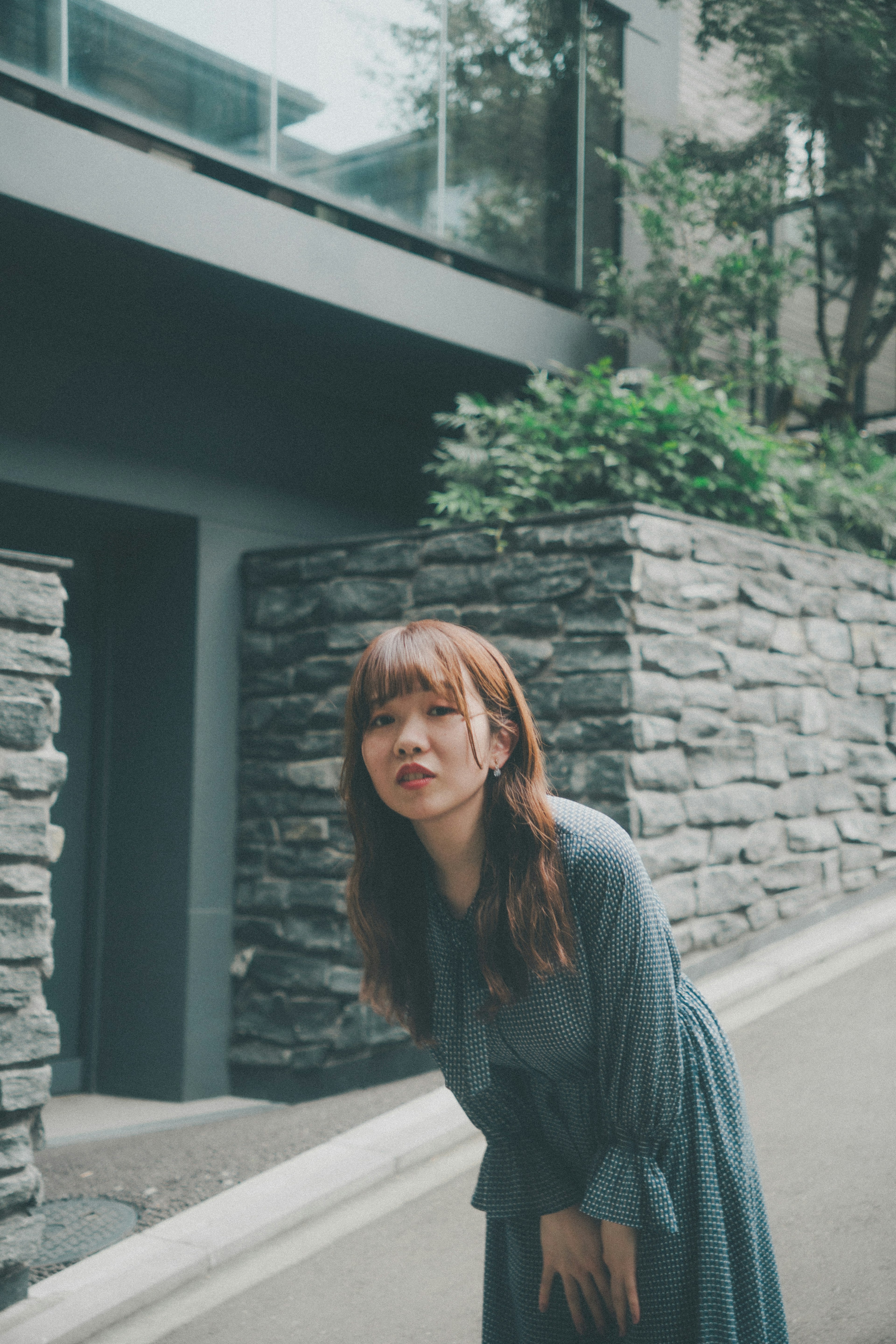 A woman in a gray dress posing in front of a stone wall