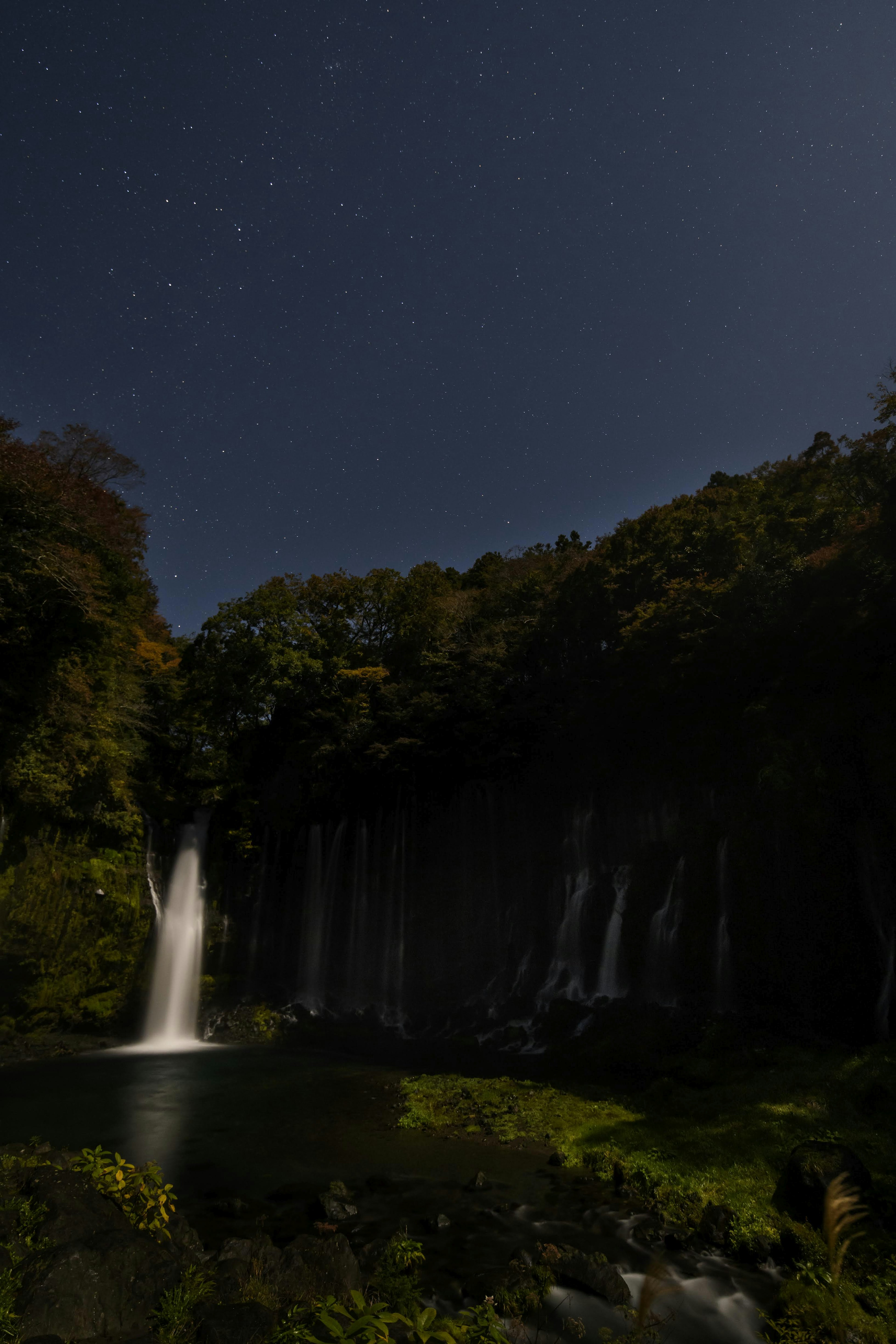 Ein Wasserfall, der im Mondlicht unter einem sternenklaren Nachthimmel leuchtet