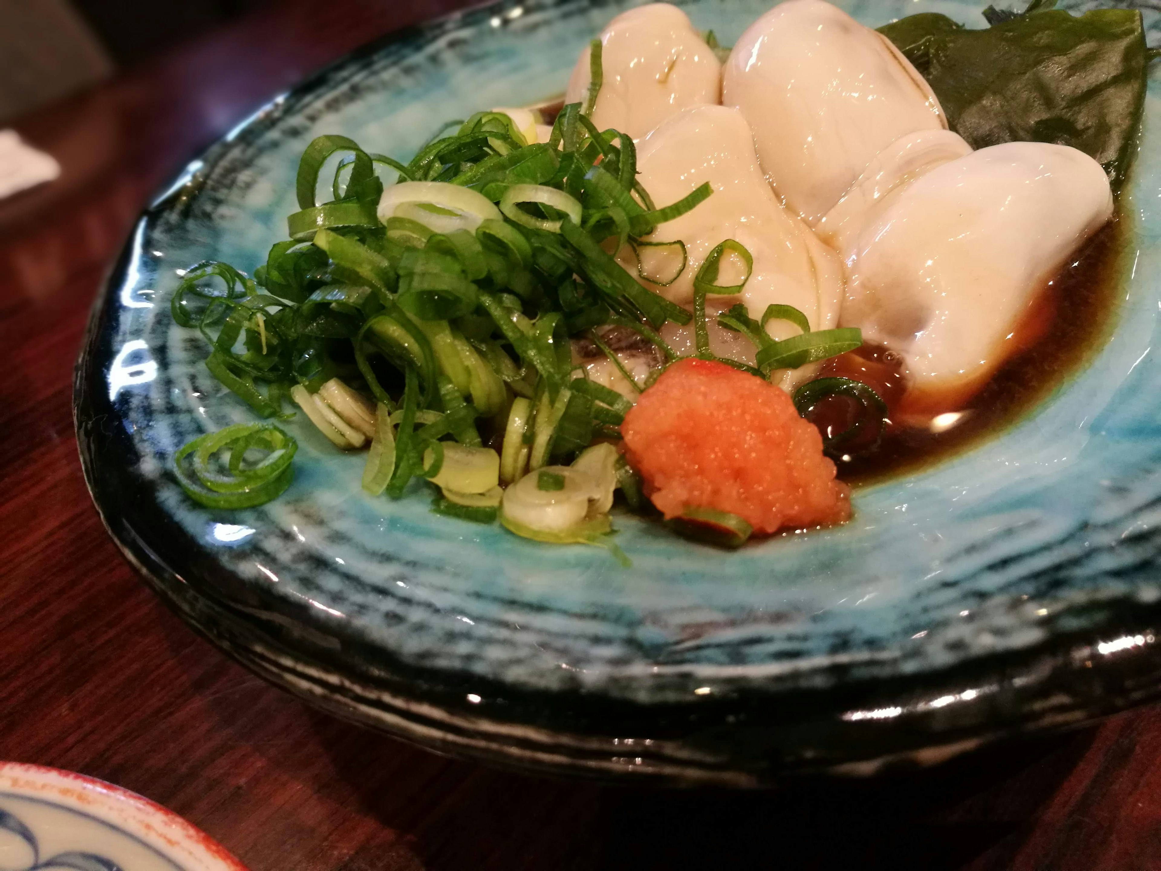 Fresh oysters served on a blue plate with green onions and wasabi