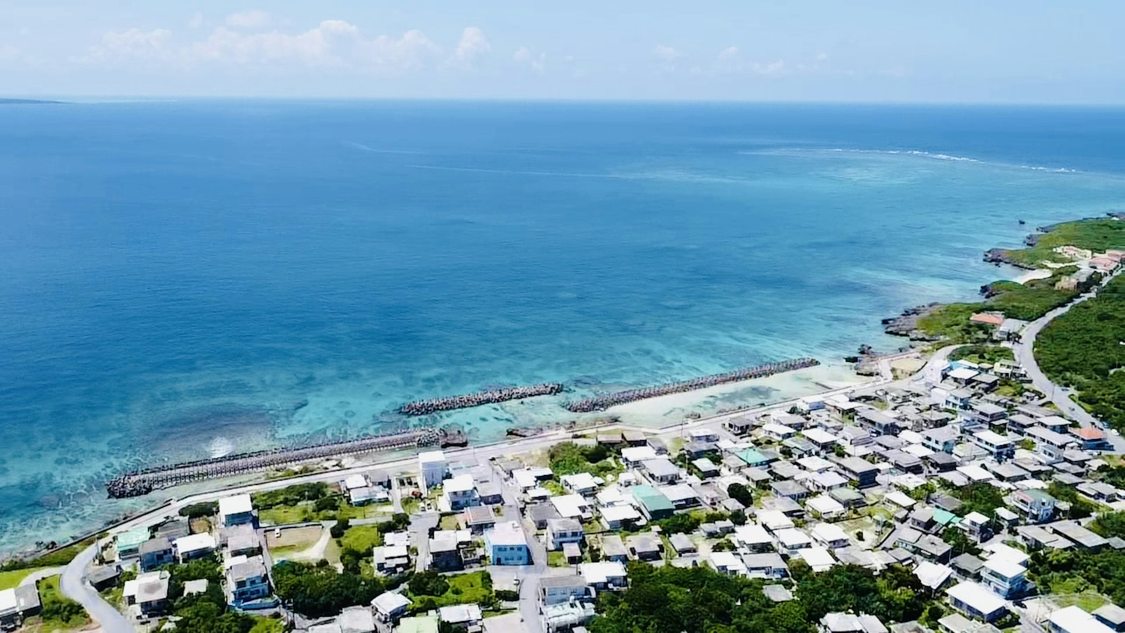 海岸村庄的航拍视图，周围环绕着蓝色海洋和白色云朵