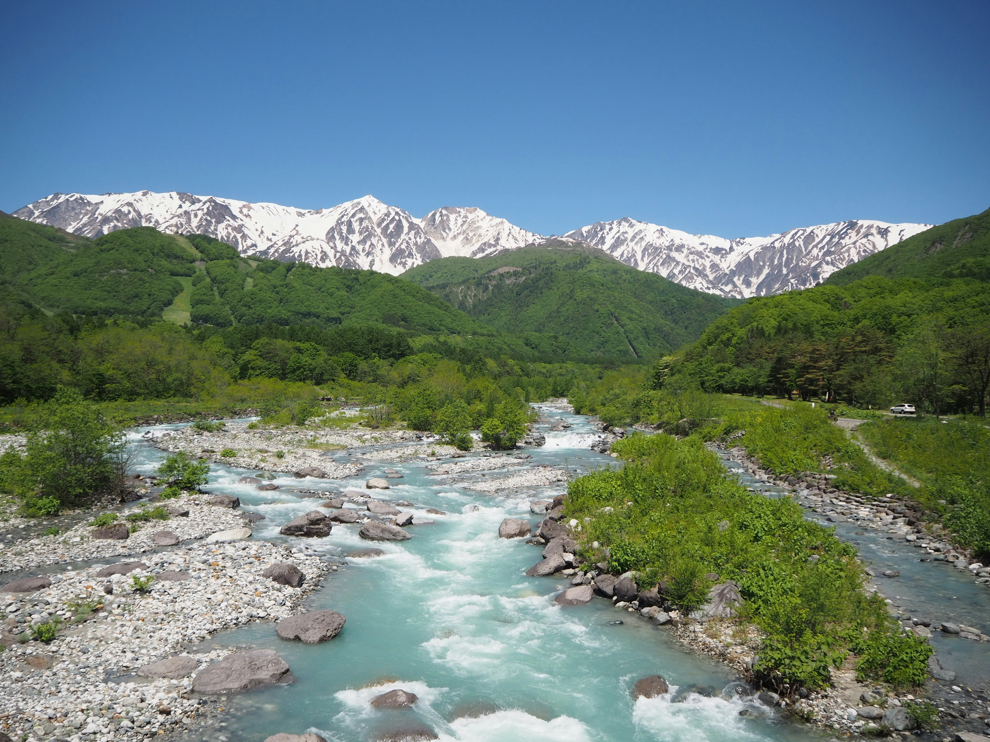 雪をかぶった山々と緑豊かな谷を流れる清流の風景