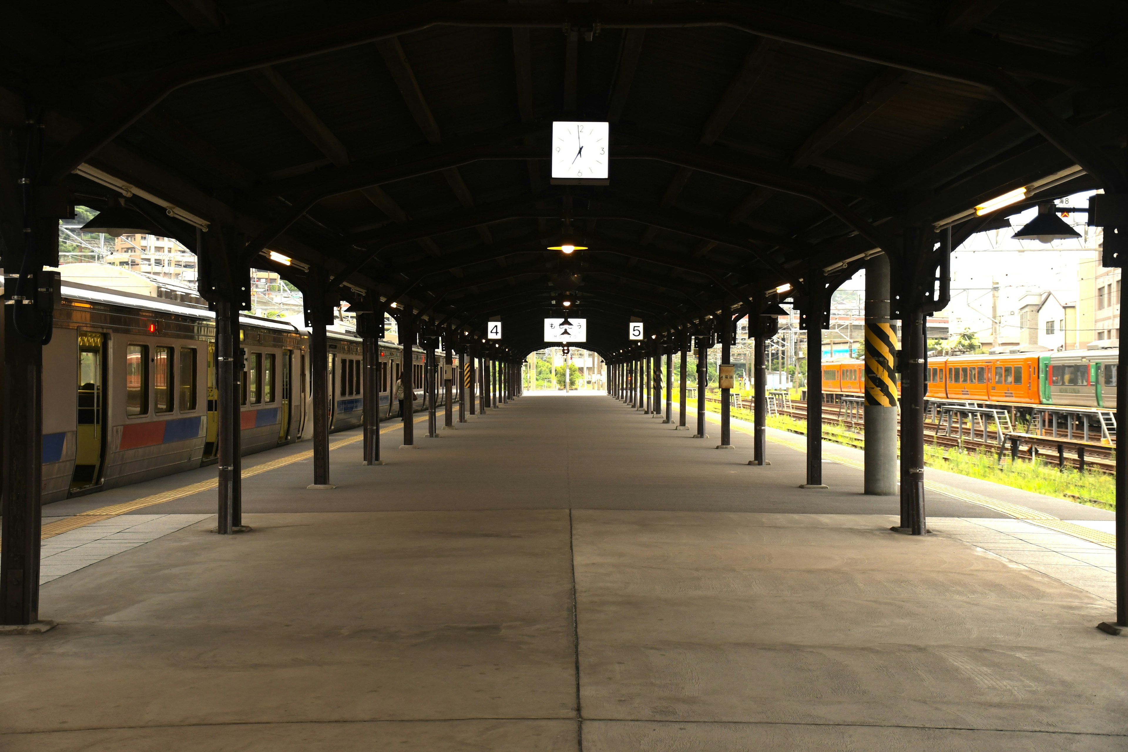 ชานชาลารถไฟกว้างพร้อมรถไฟที่เรียงกันและโครงสร้างหลังคา