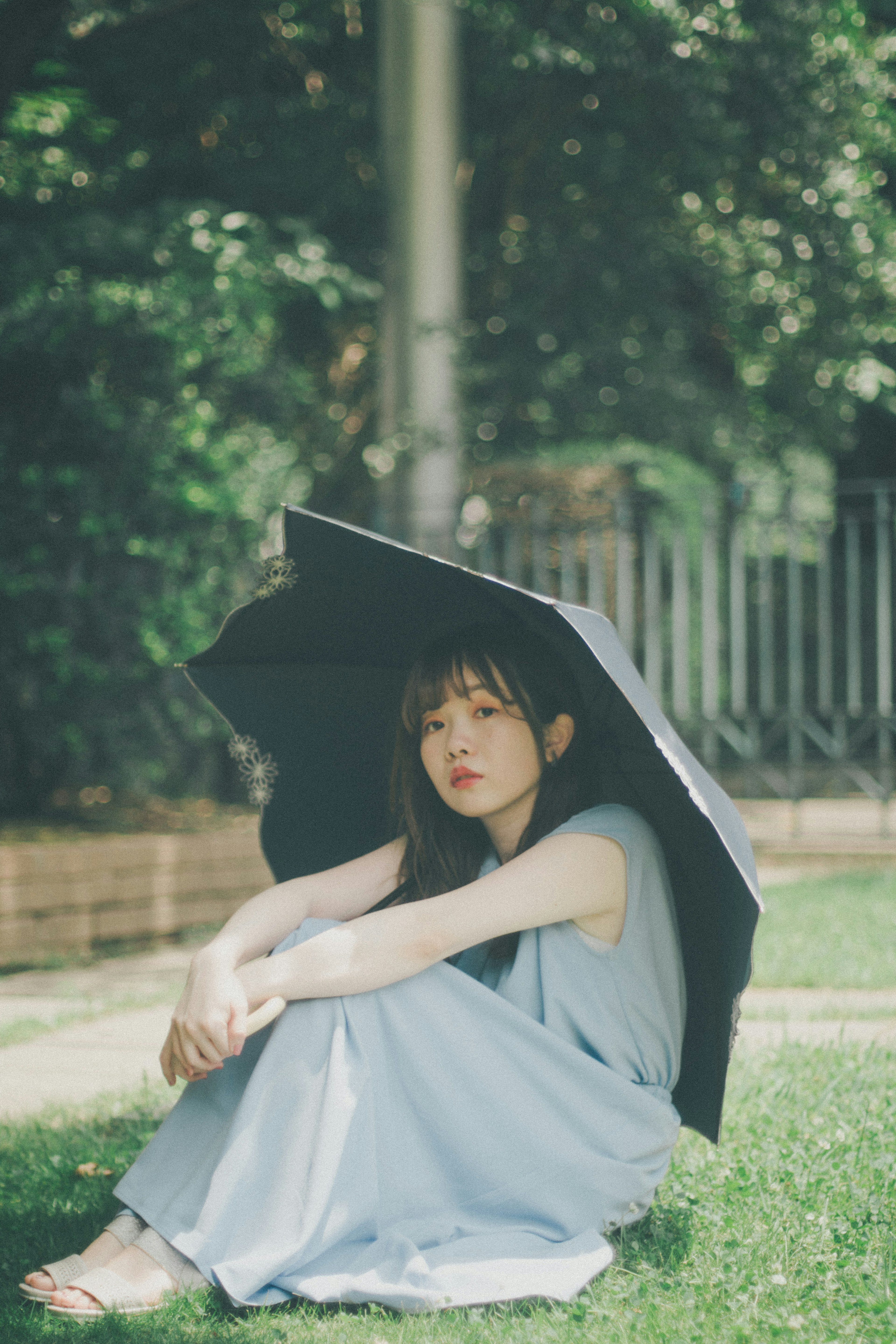 A woman sitting with a black umbrella in a green outdoor setting