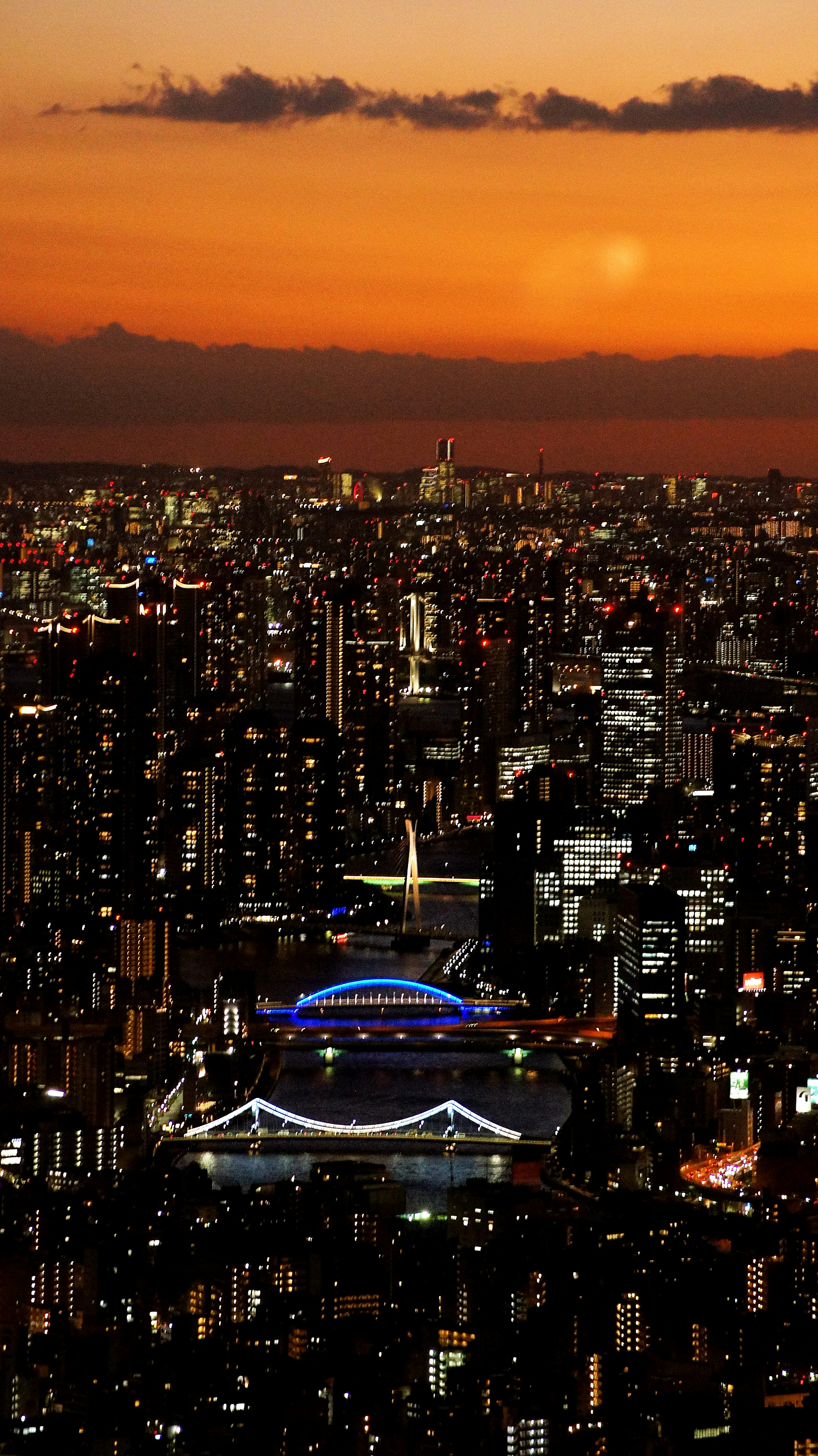 Skyline della città al tramonto con edifici illuminati e uno stadio colorato sotto un cielo vibrante