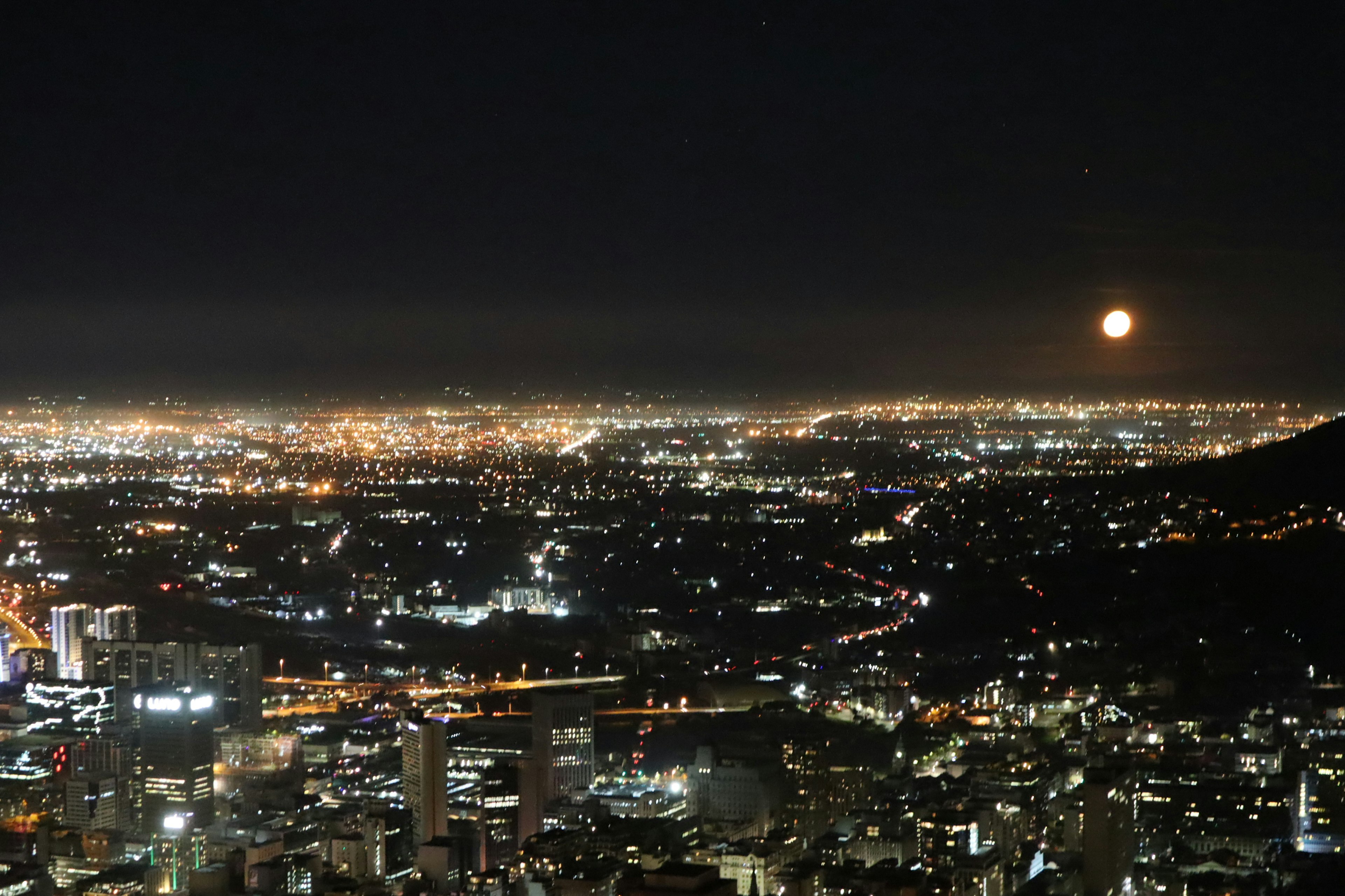 Night view of a cityscape with mountains and a rising moon