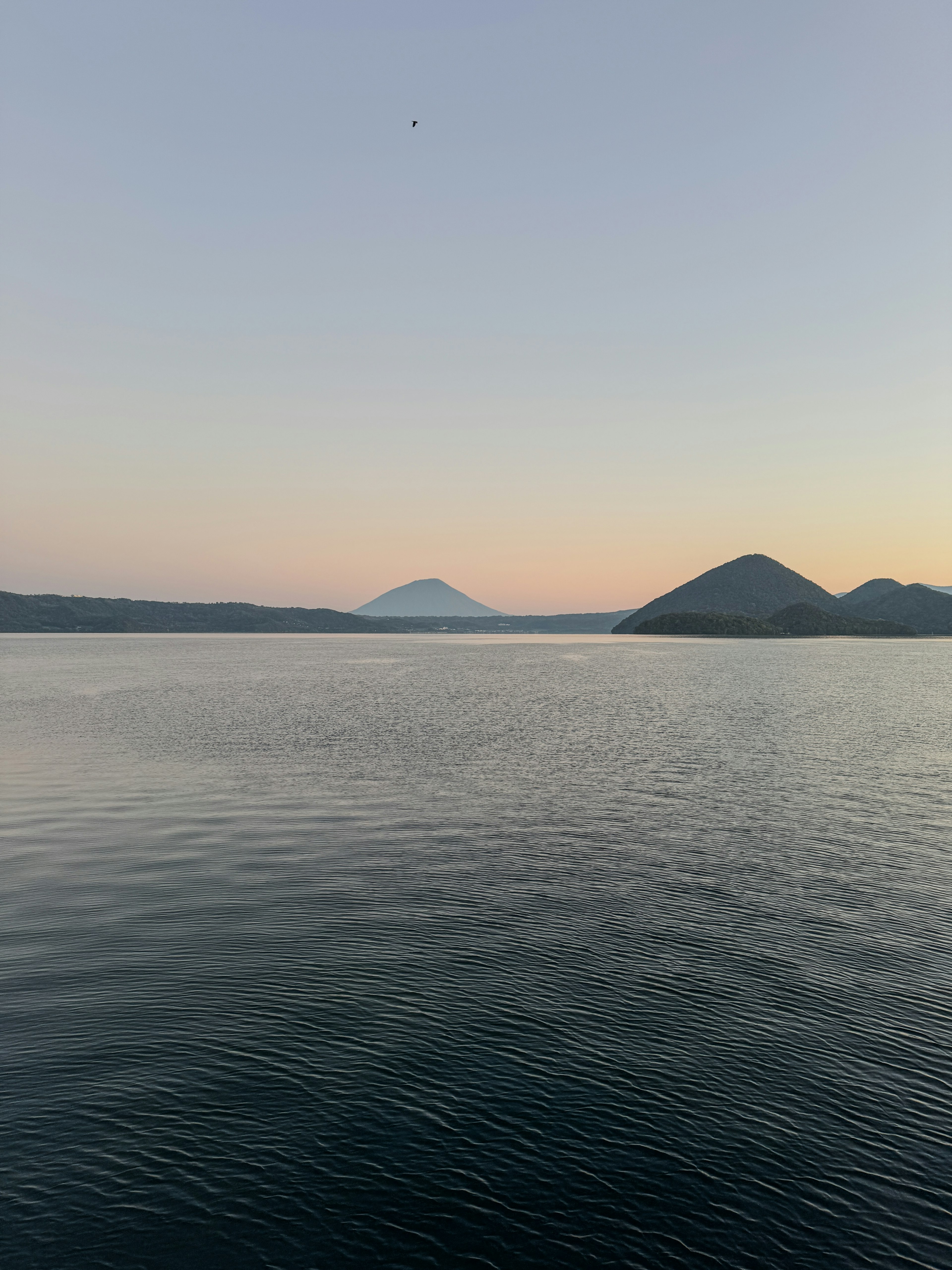 Permukaan air tenang dengan siluet gunung saat matahari terbenam