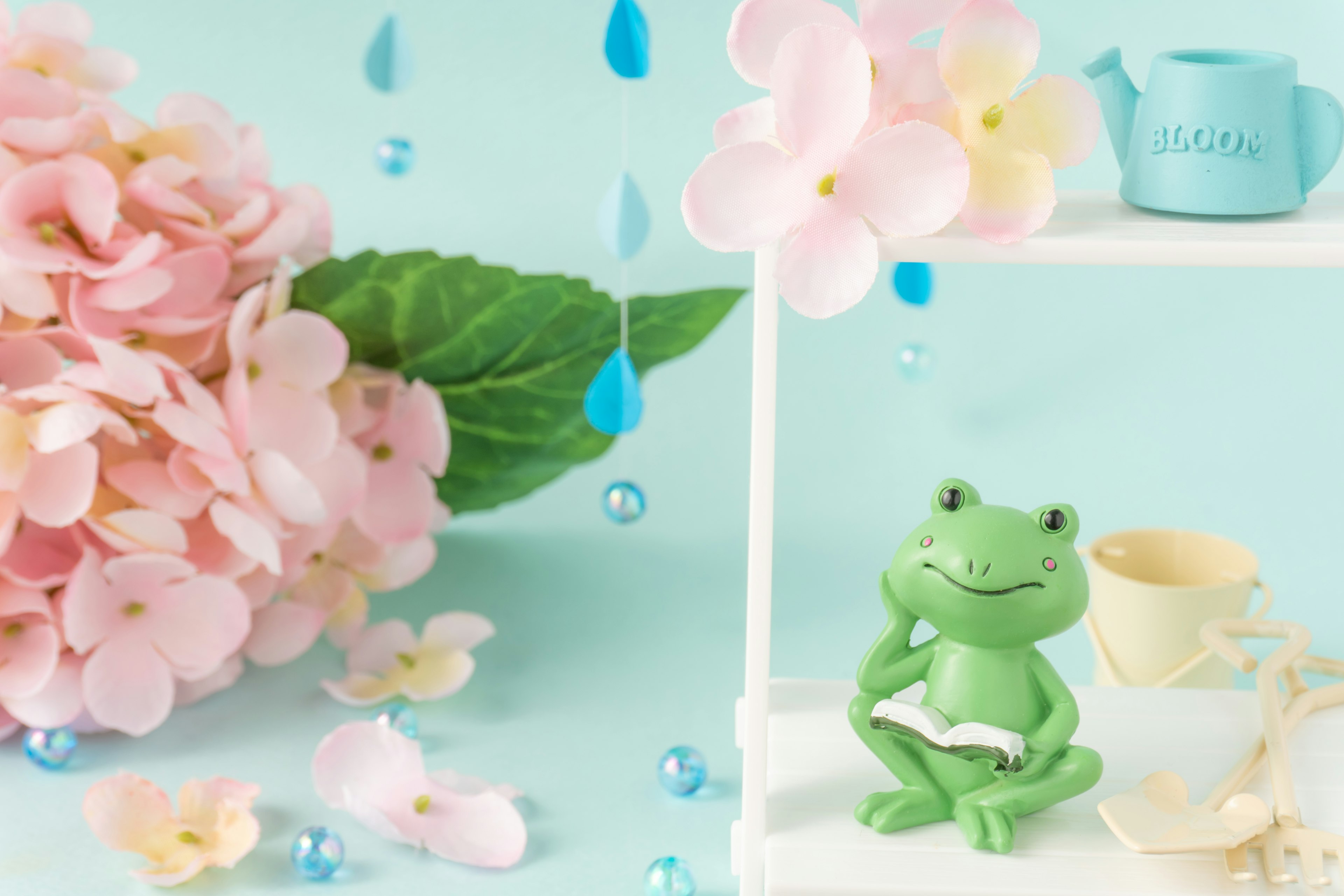 Une figurine de grenouille assise sur une étagère avec des fleurs roses et des décorations bleues