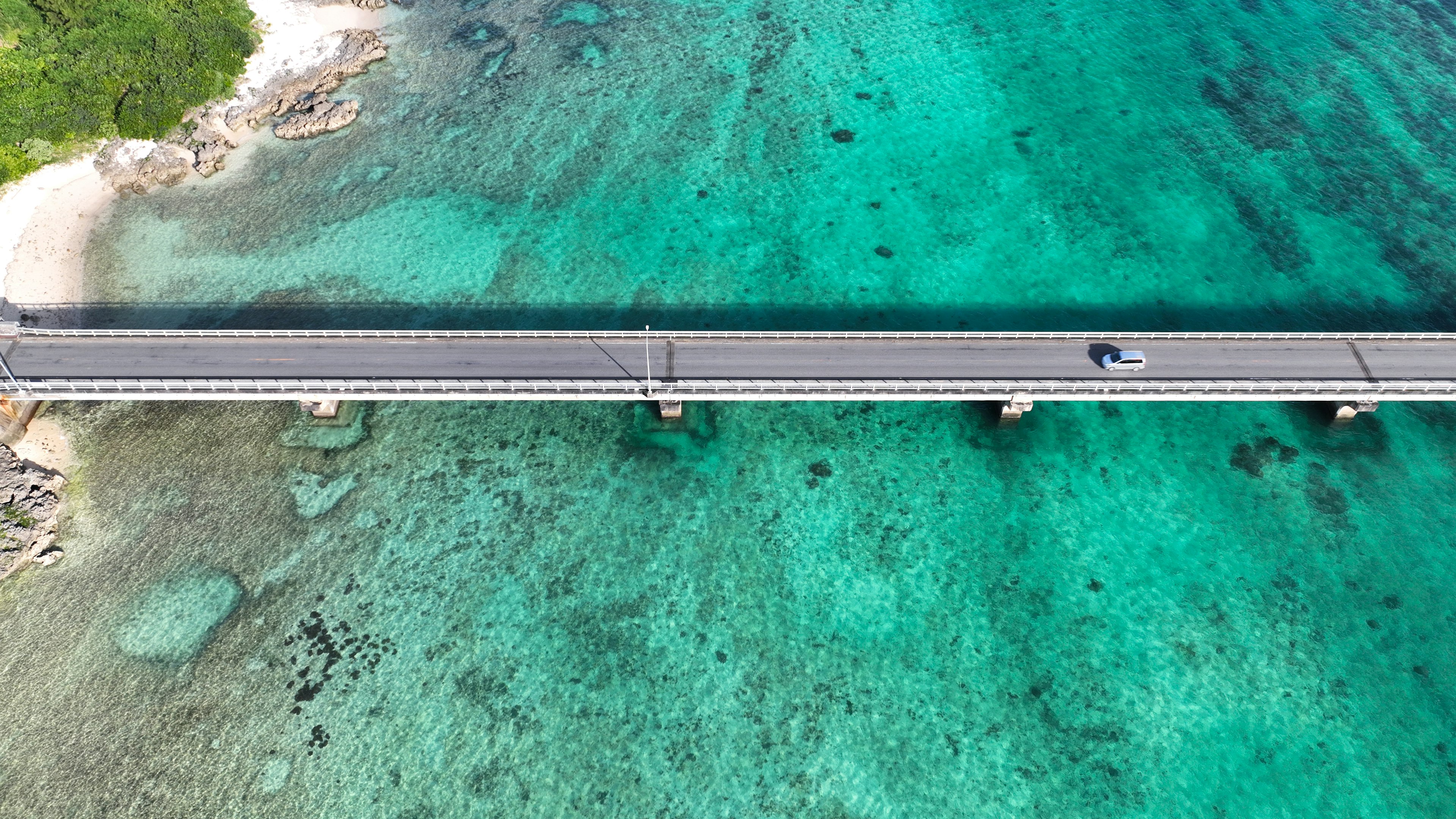 Aerial view of a bridge over turquoise water with a car