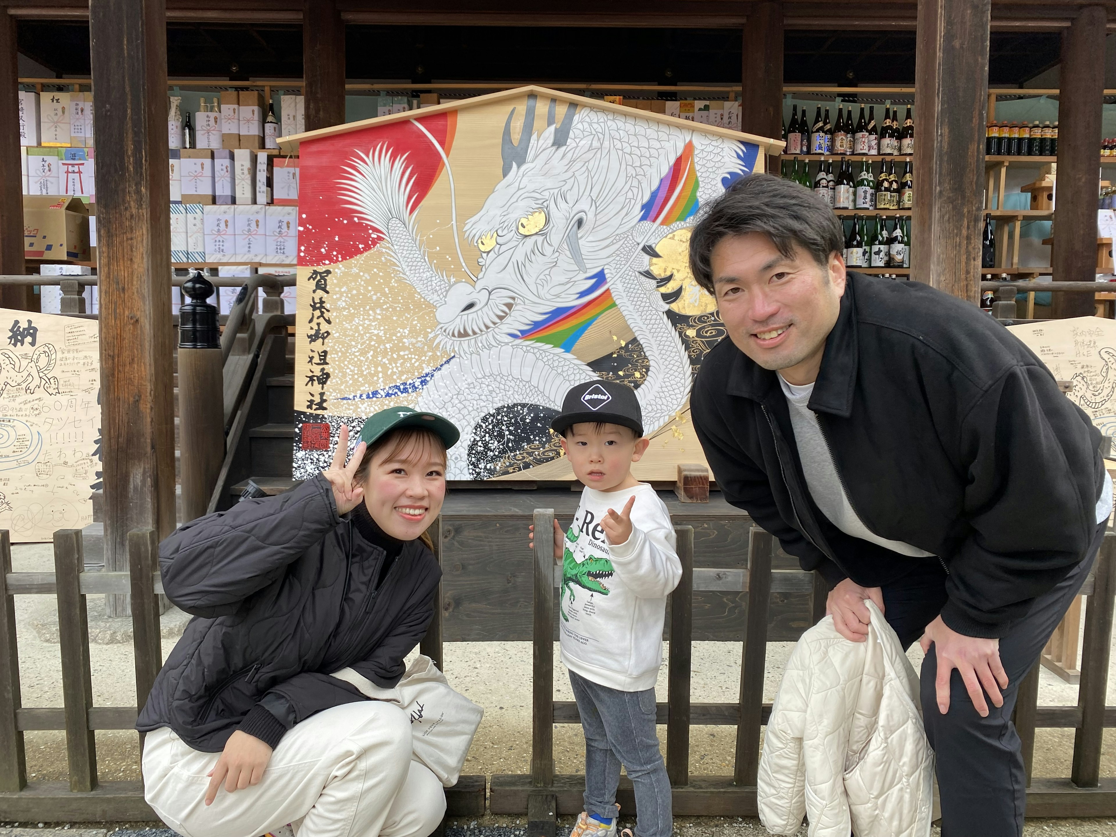 家族が神社の前でポーズをとる子供と大人の写真 伝統的なアートワークが背景にある