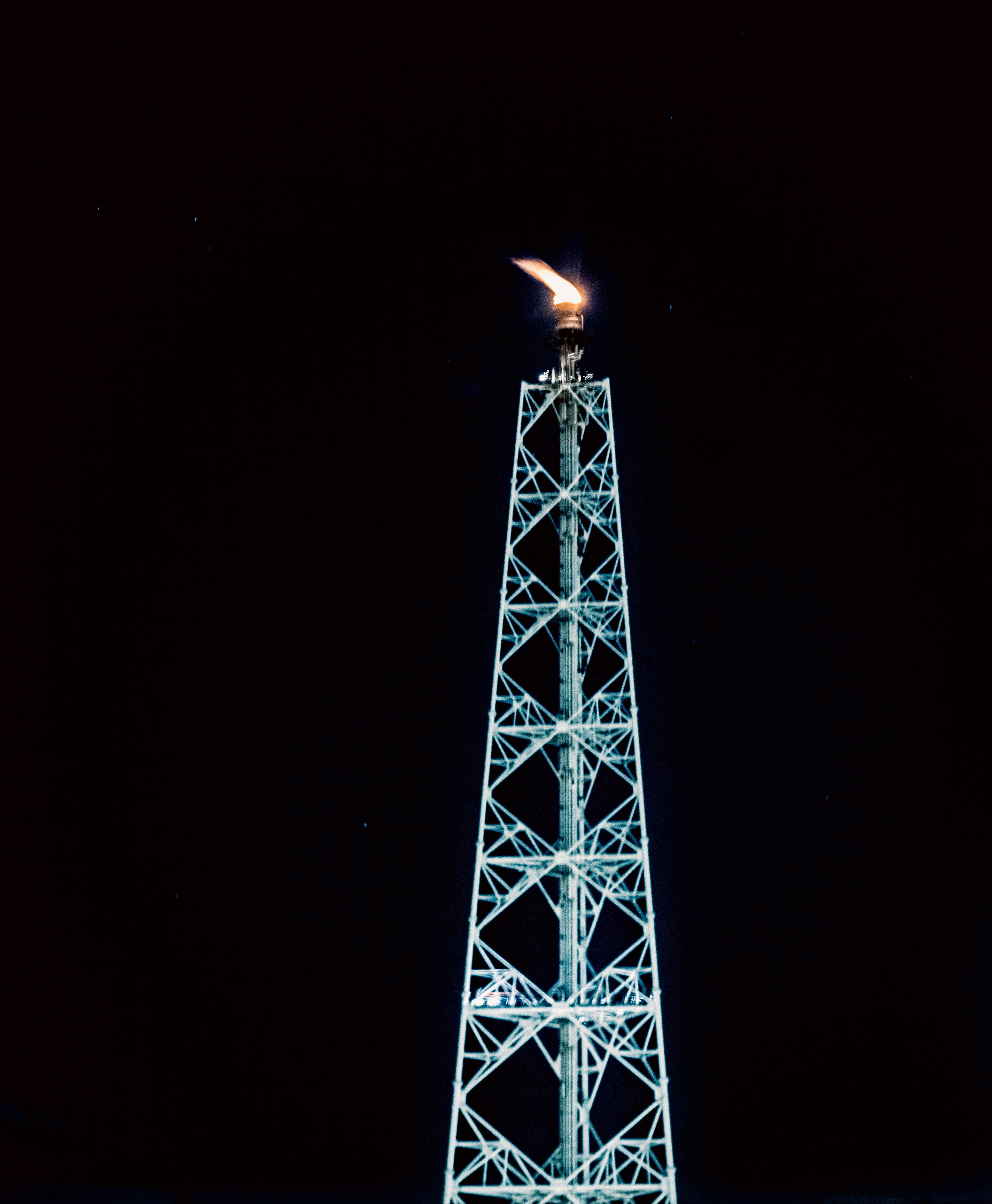 Una alta torre in acciaio illuminata da fiamme contro un cielo scuro