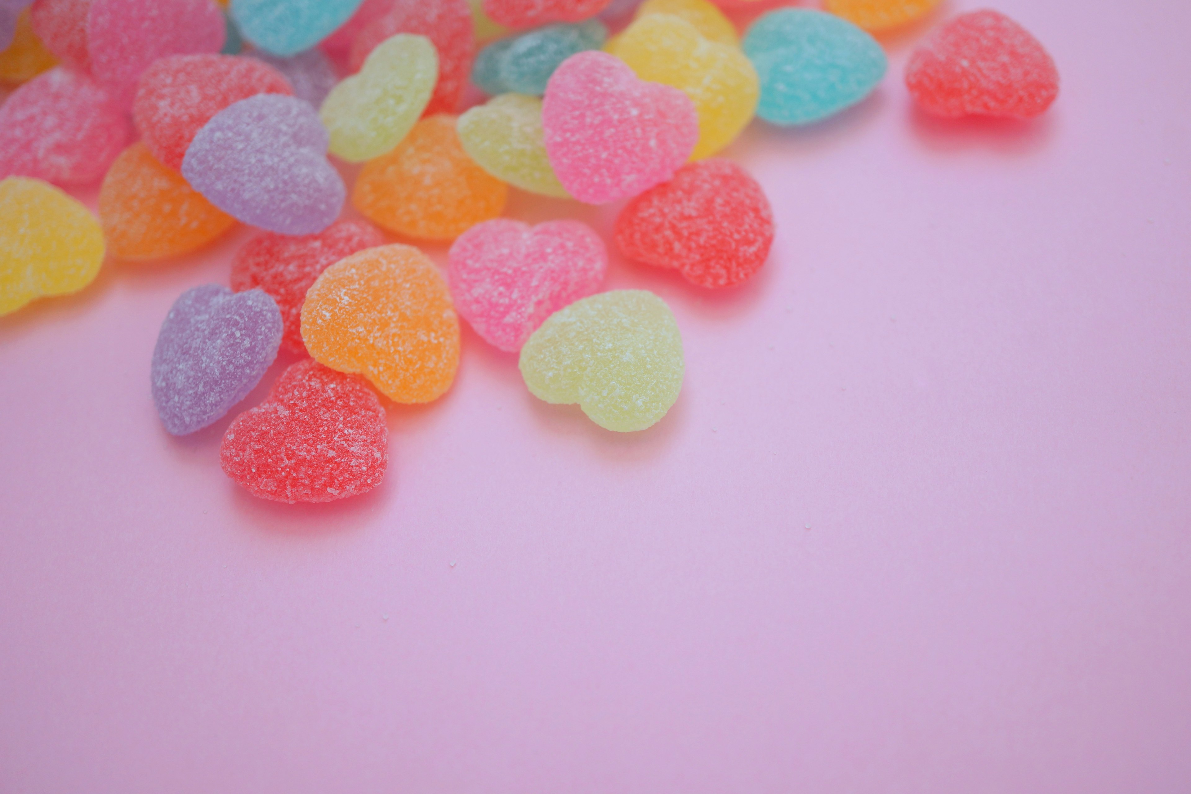 Colorful heart-shaped gummy candies scattered on a pink background