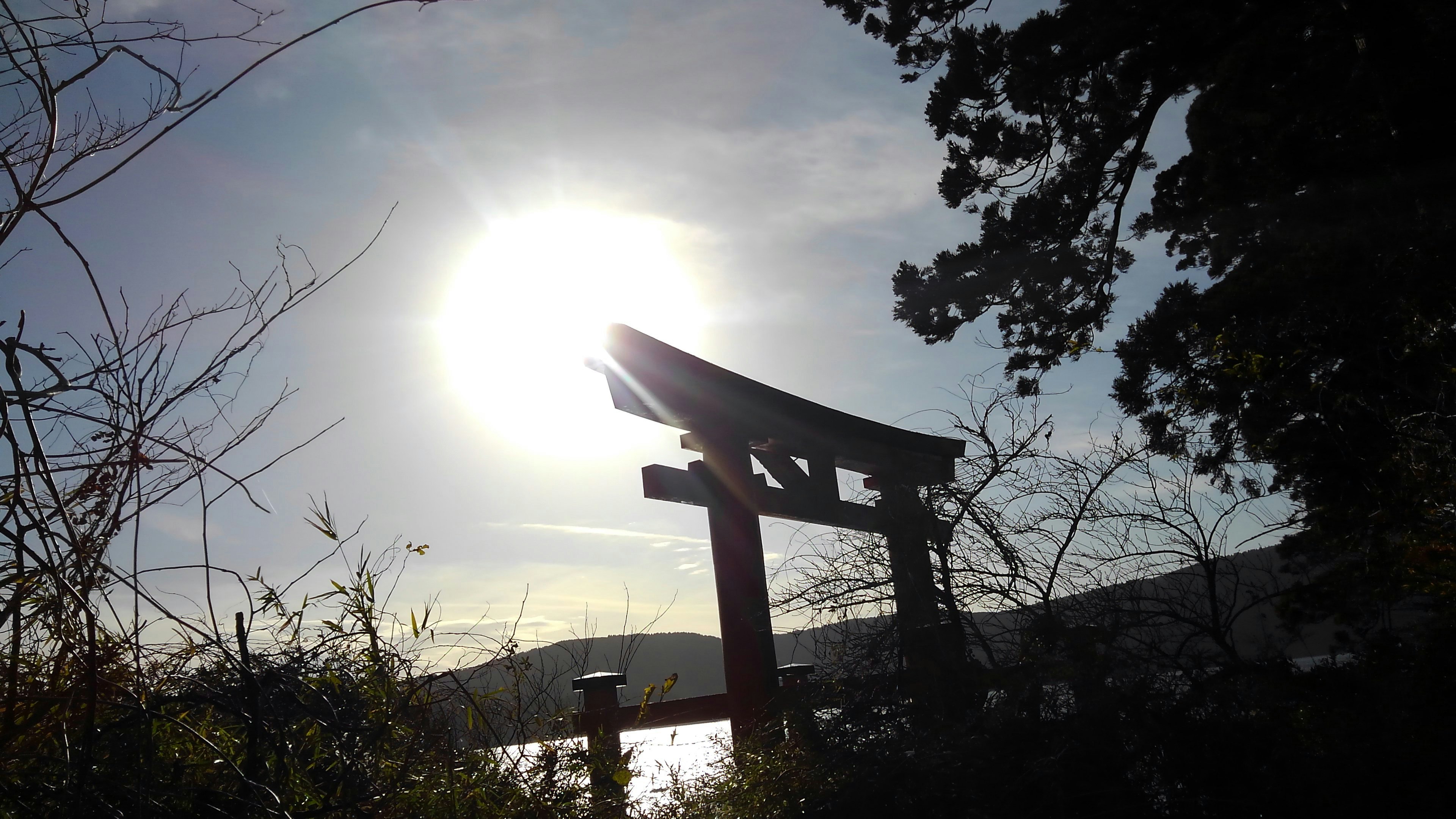 Torii-Tor silhouettiert gegen die Sonne mit natürlicher Landschaft