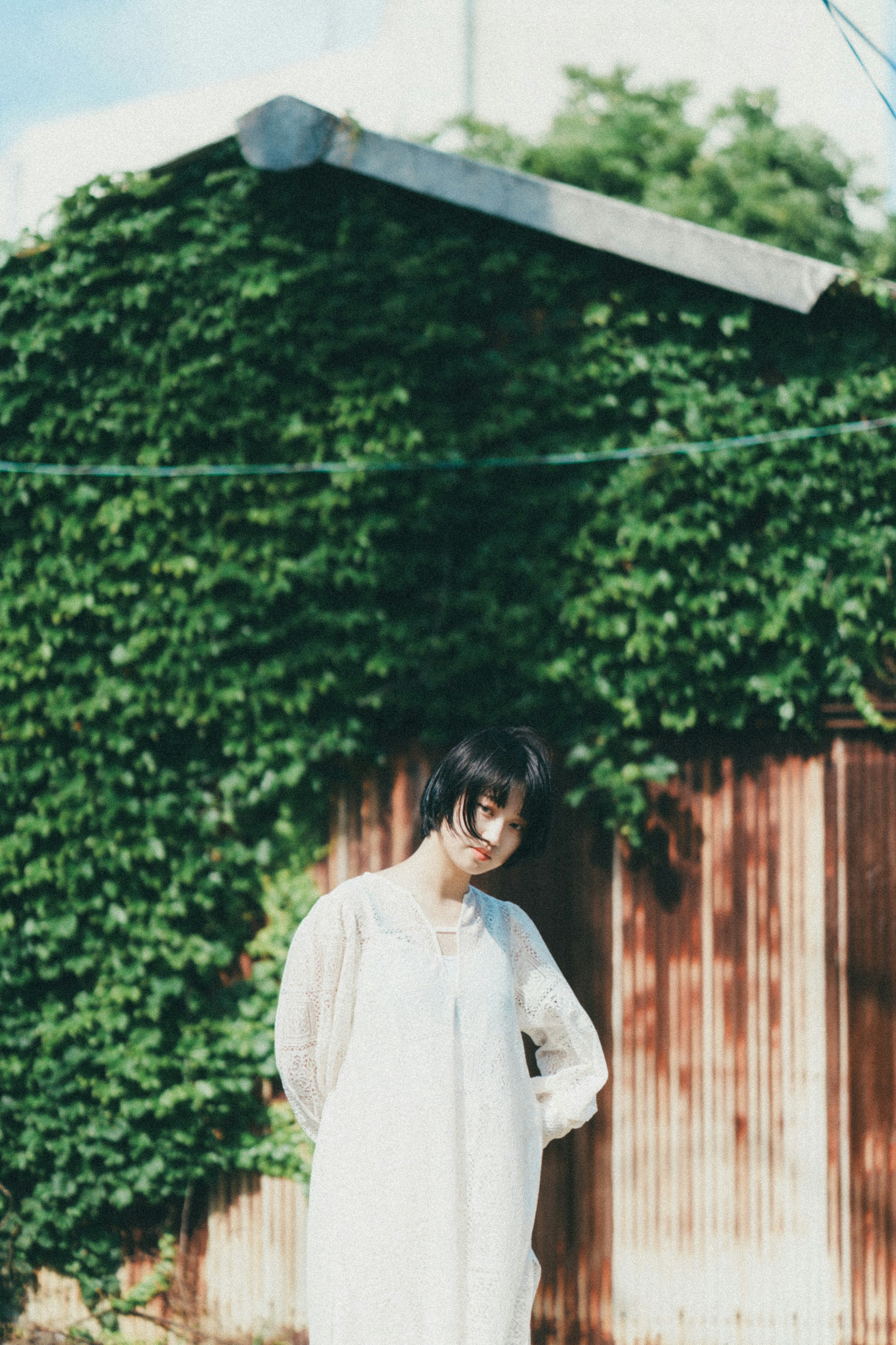 Woman standing in front of a wooden fence covered in green ivy