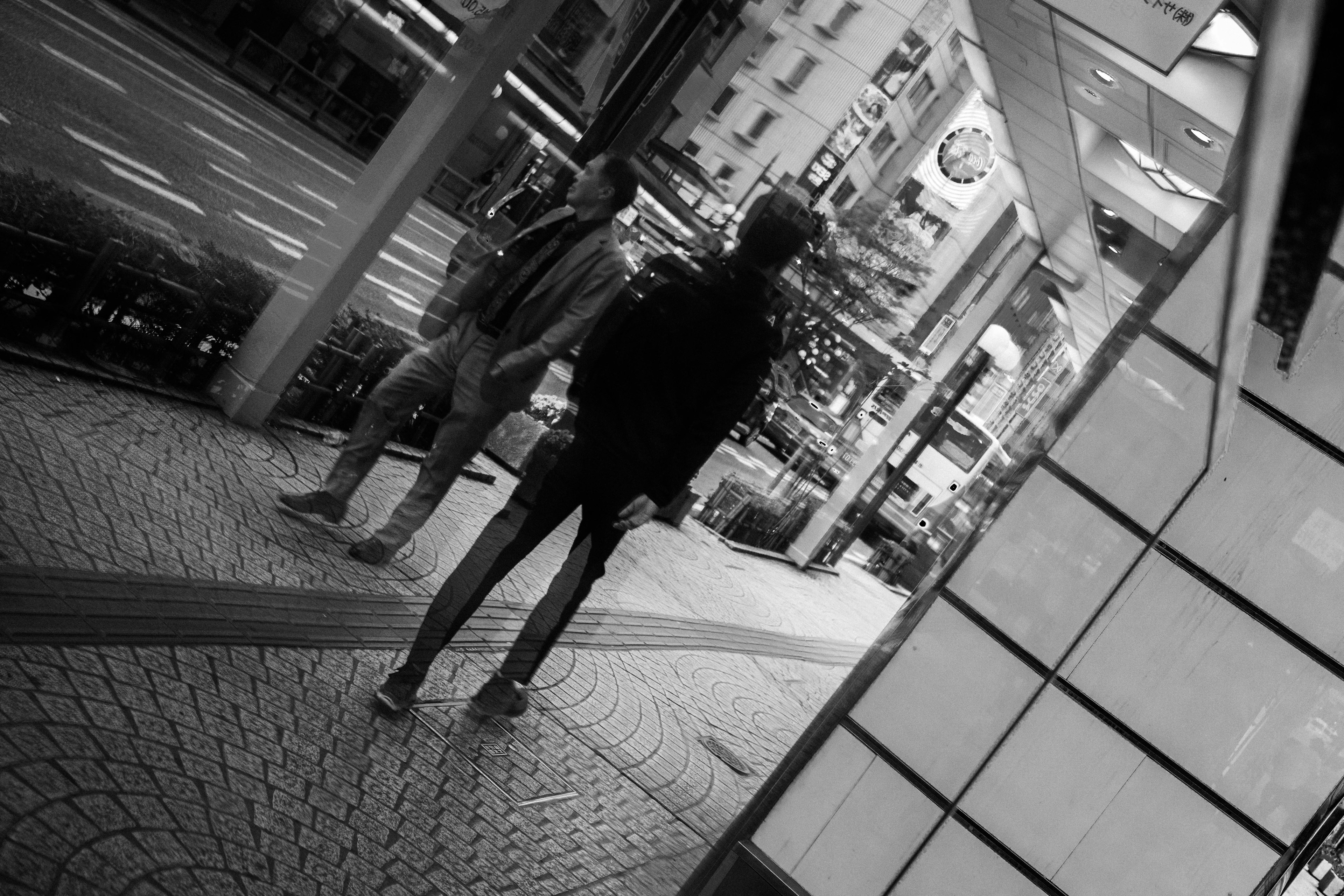 Dos personas de pie en una esquina de la calle con un paisaje urbano en blanco y negro