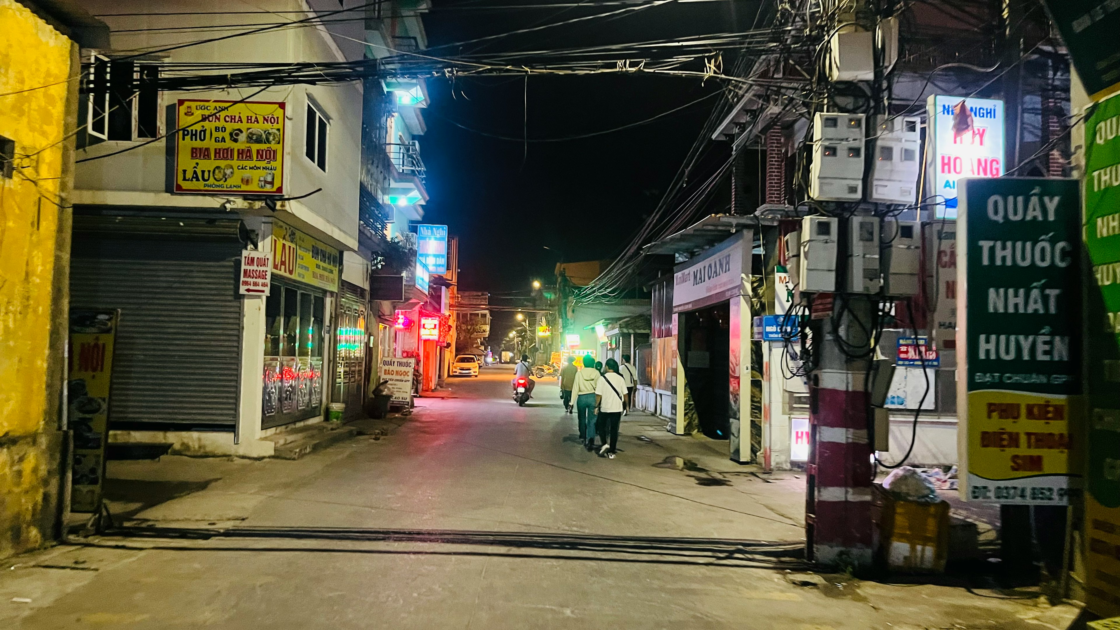 夜の街道に沿った商業エリアの風景 明るいネオン看板と電線が交差する様子