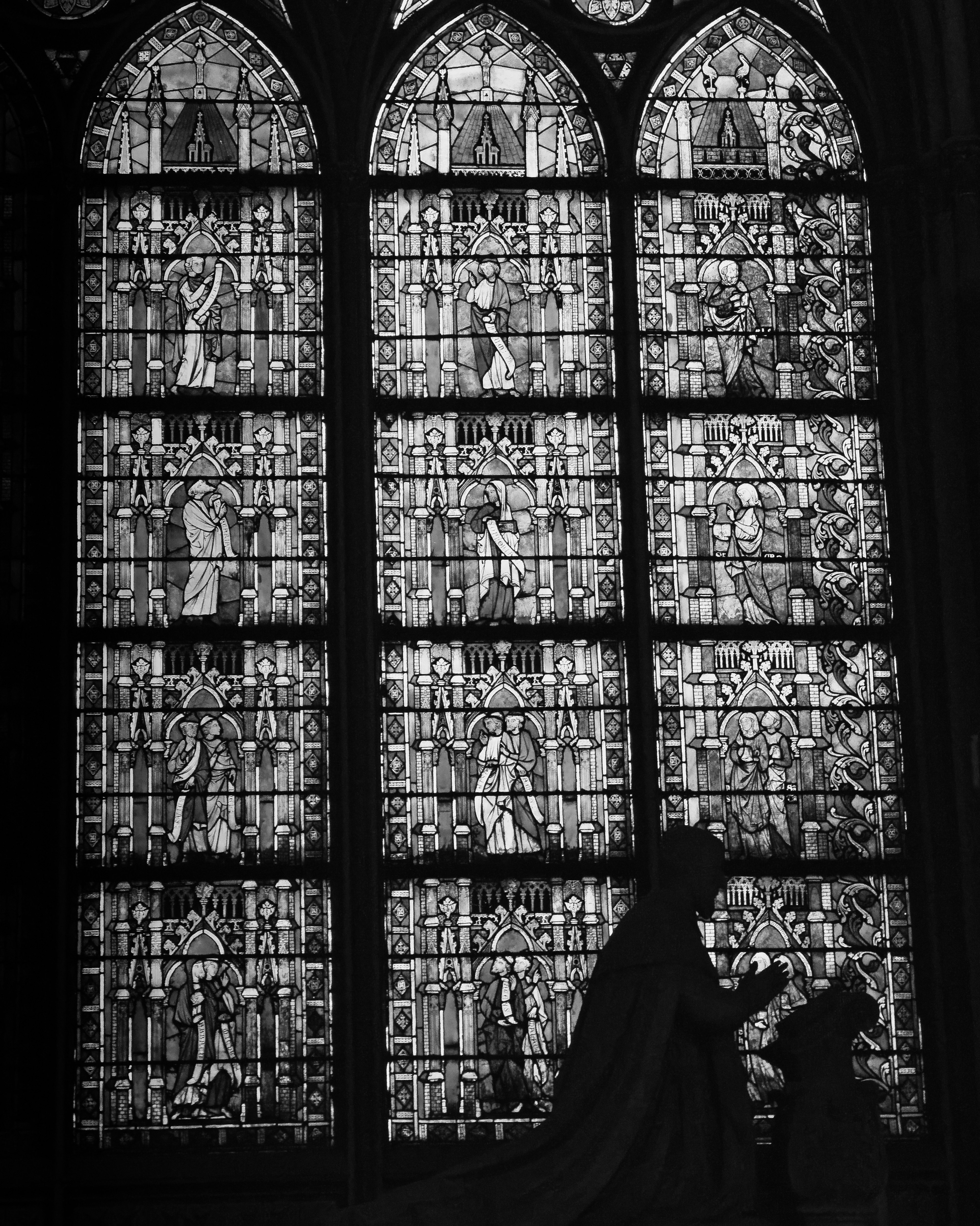 Silhouette of individuals praying in front of church stained glass windows