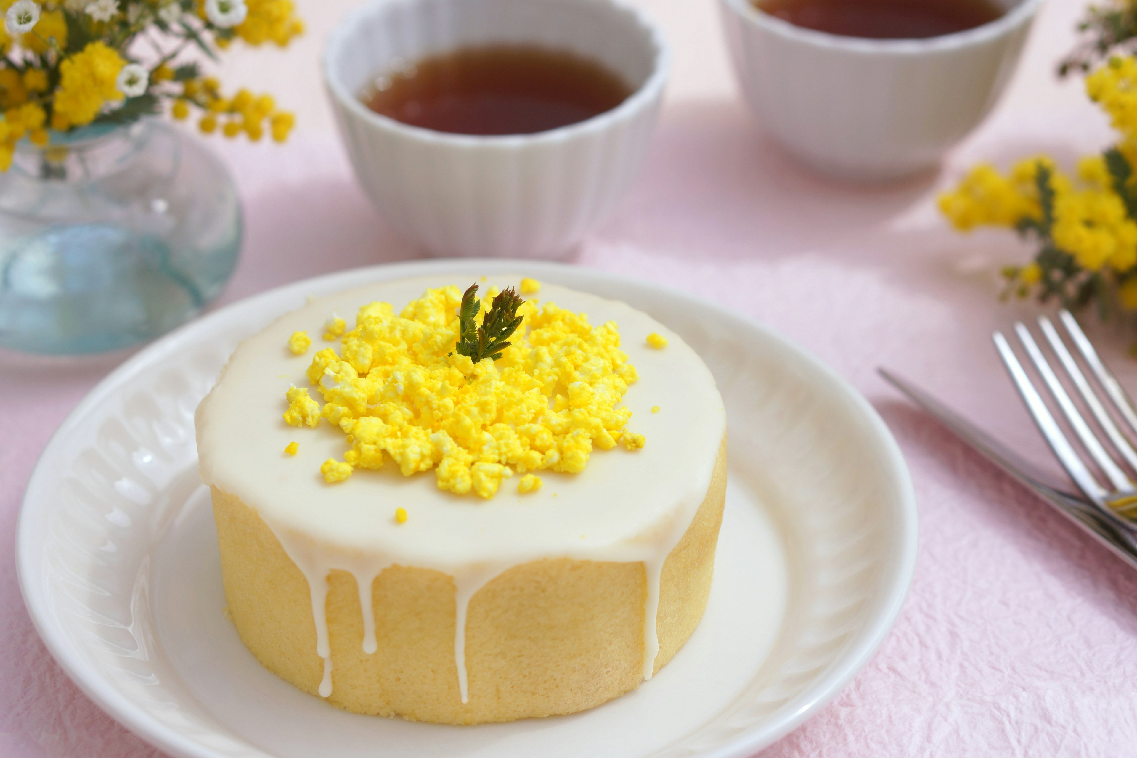 Un pastel con cobertura amarilla y tazas de té en una mesa de colores suaves