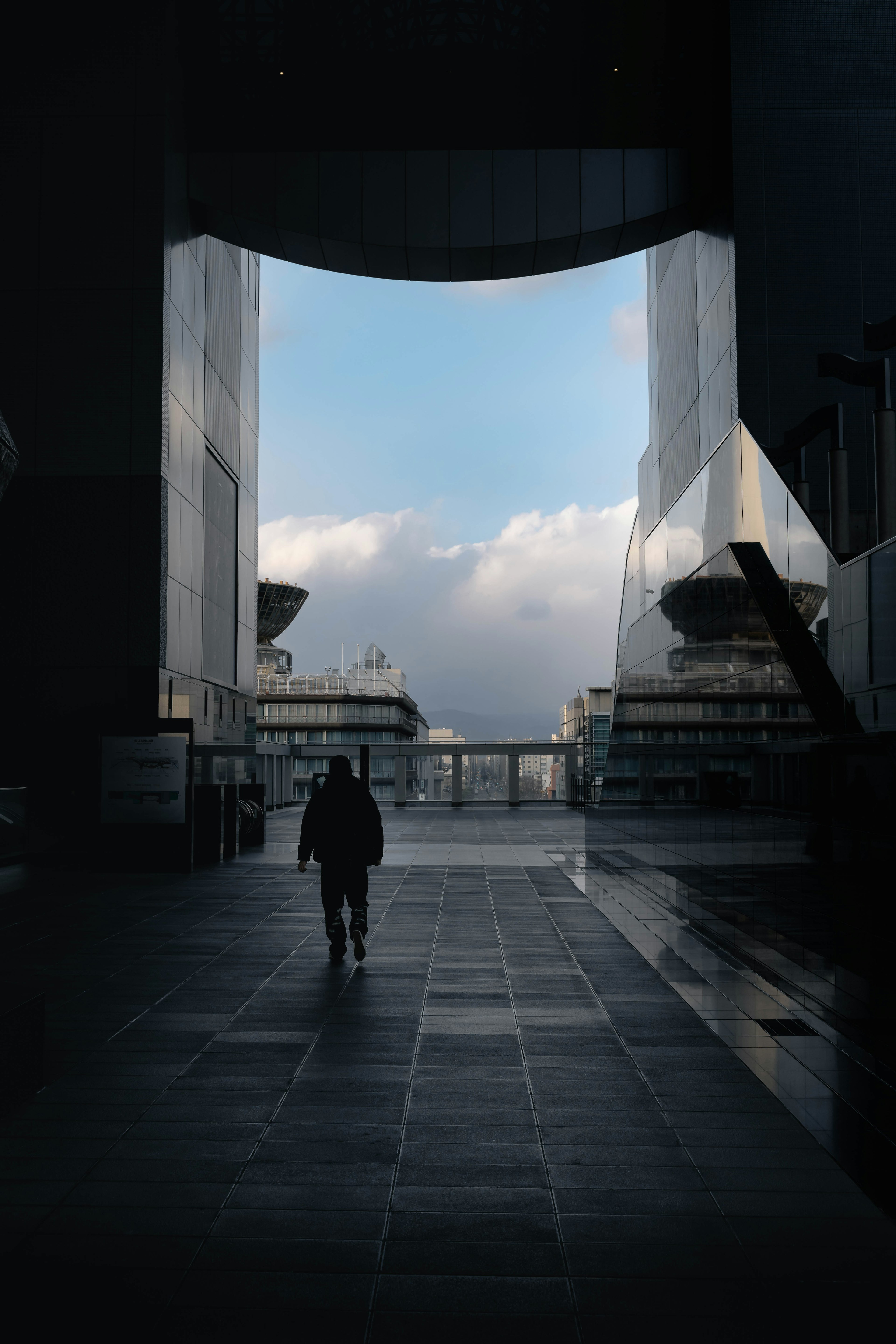 Silhouette de una persona caminando a través de una estructura moderna con cielo azul