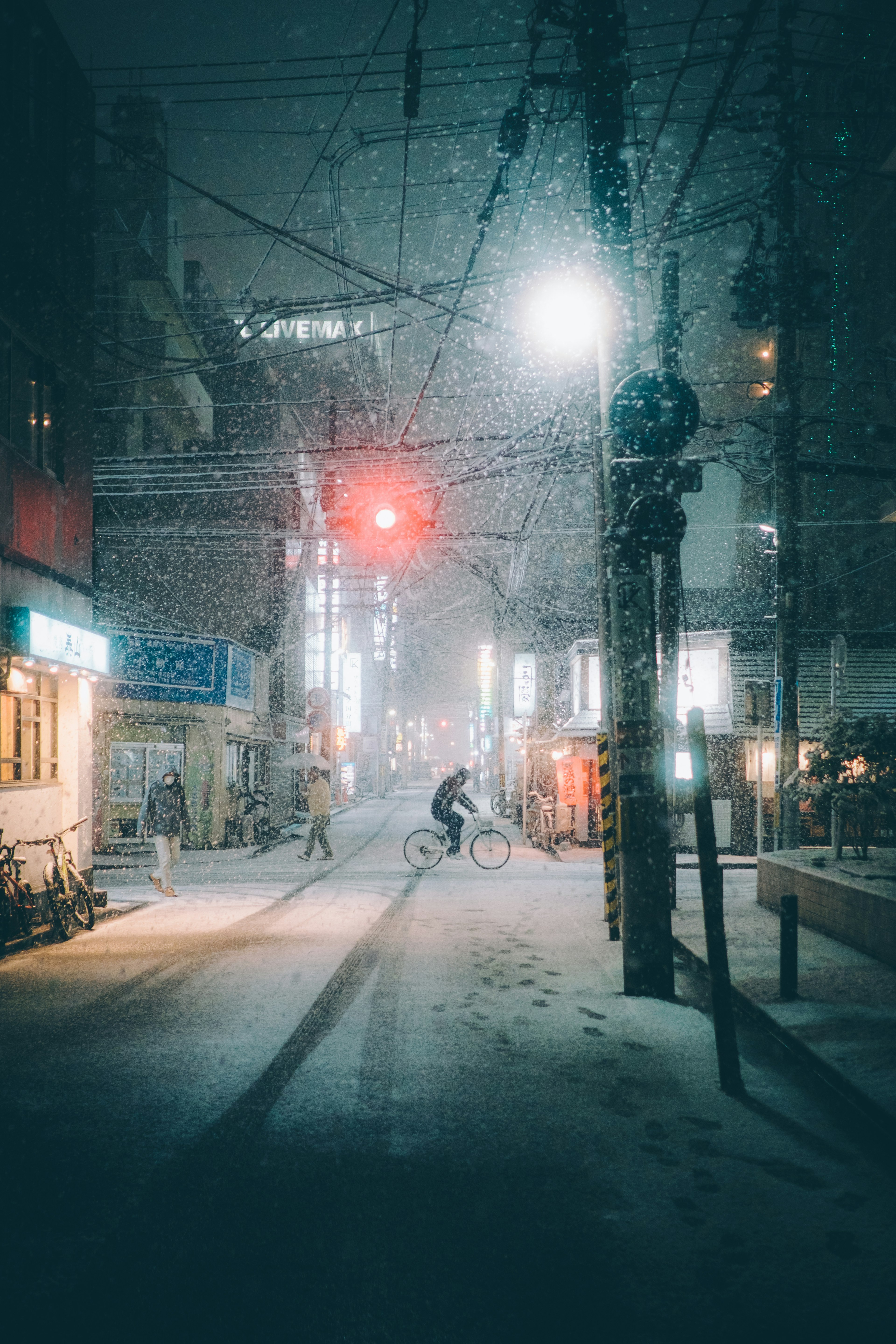 Una persona montando una bicicleta en una calle nevada de noche con un semáforo rojo