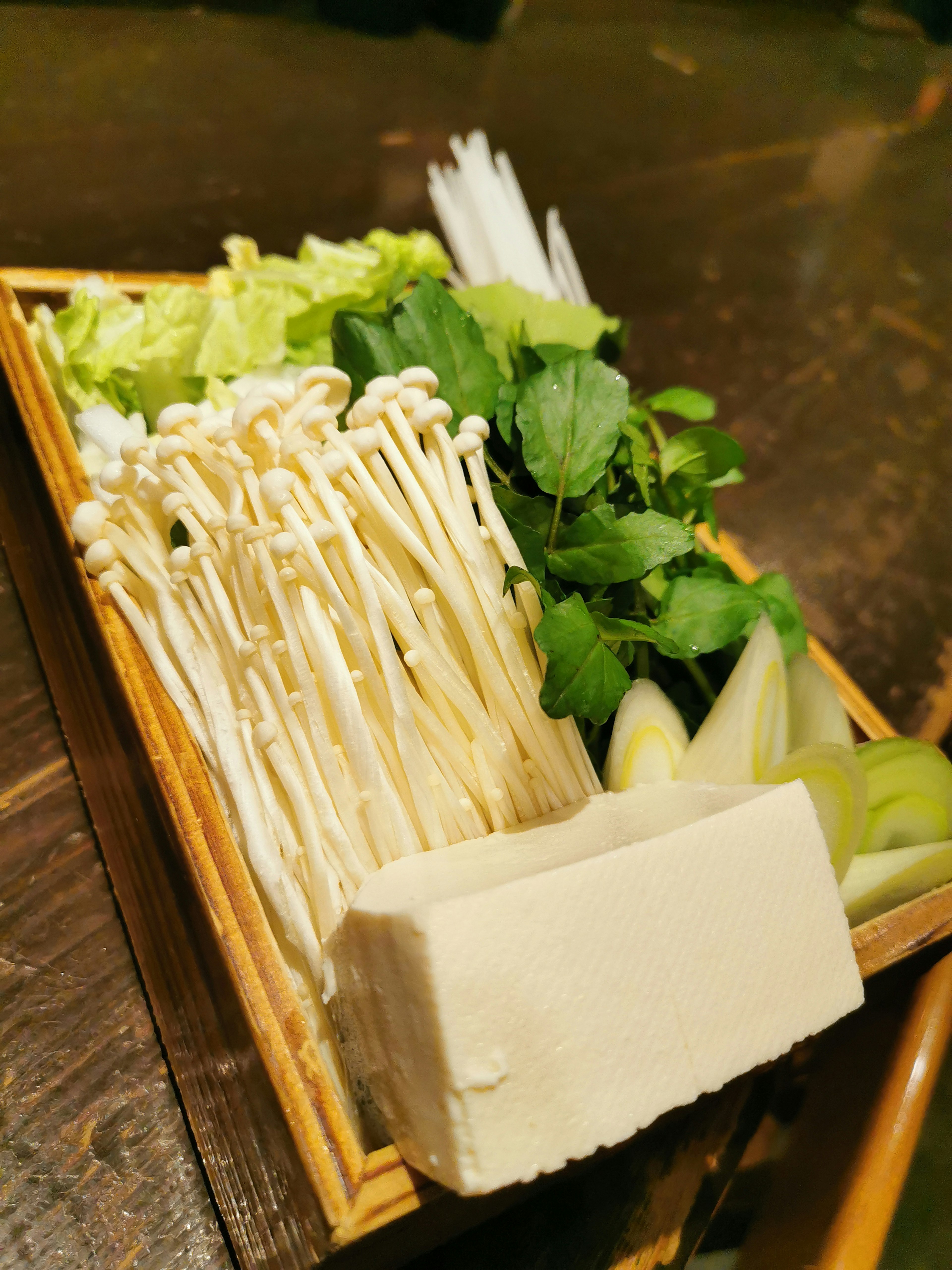 Fresh vegetables and tofu arranged in a wooden tray