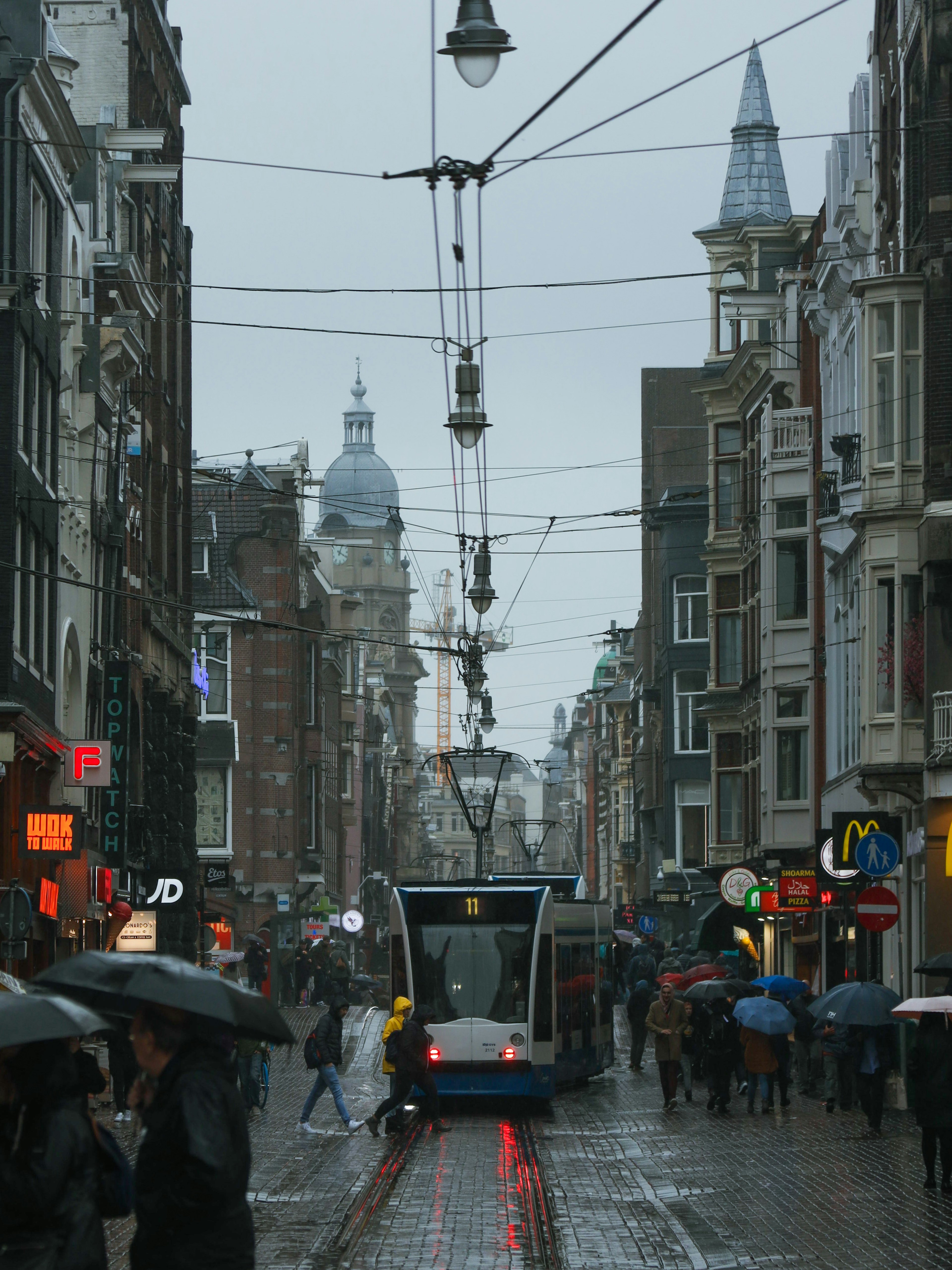 Scena di strada ad Amsterdam con tram e pedoni sotto la pioggia