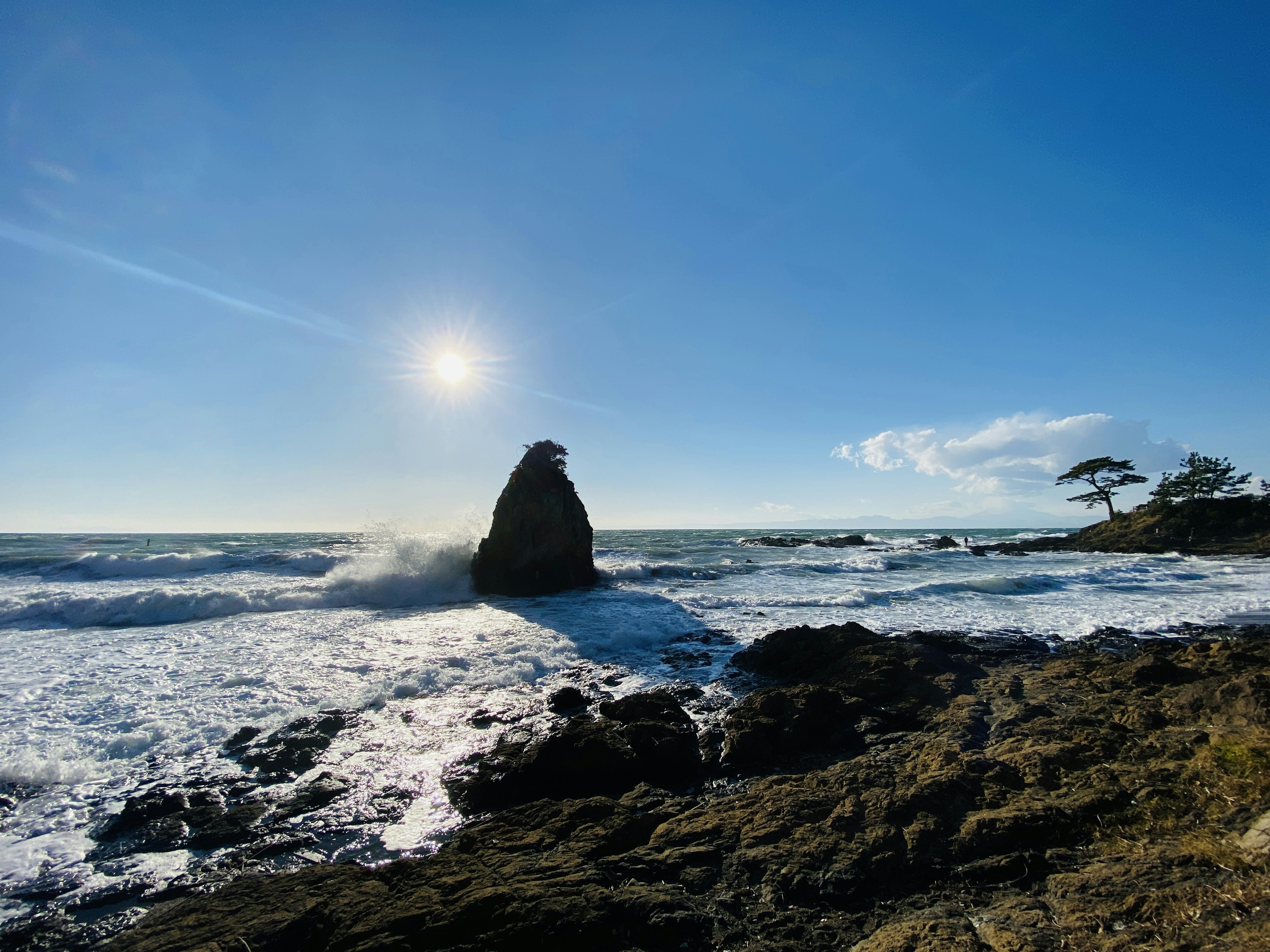 Coastal landscape with blue sky and crashing waves prominent rock and sunlight